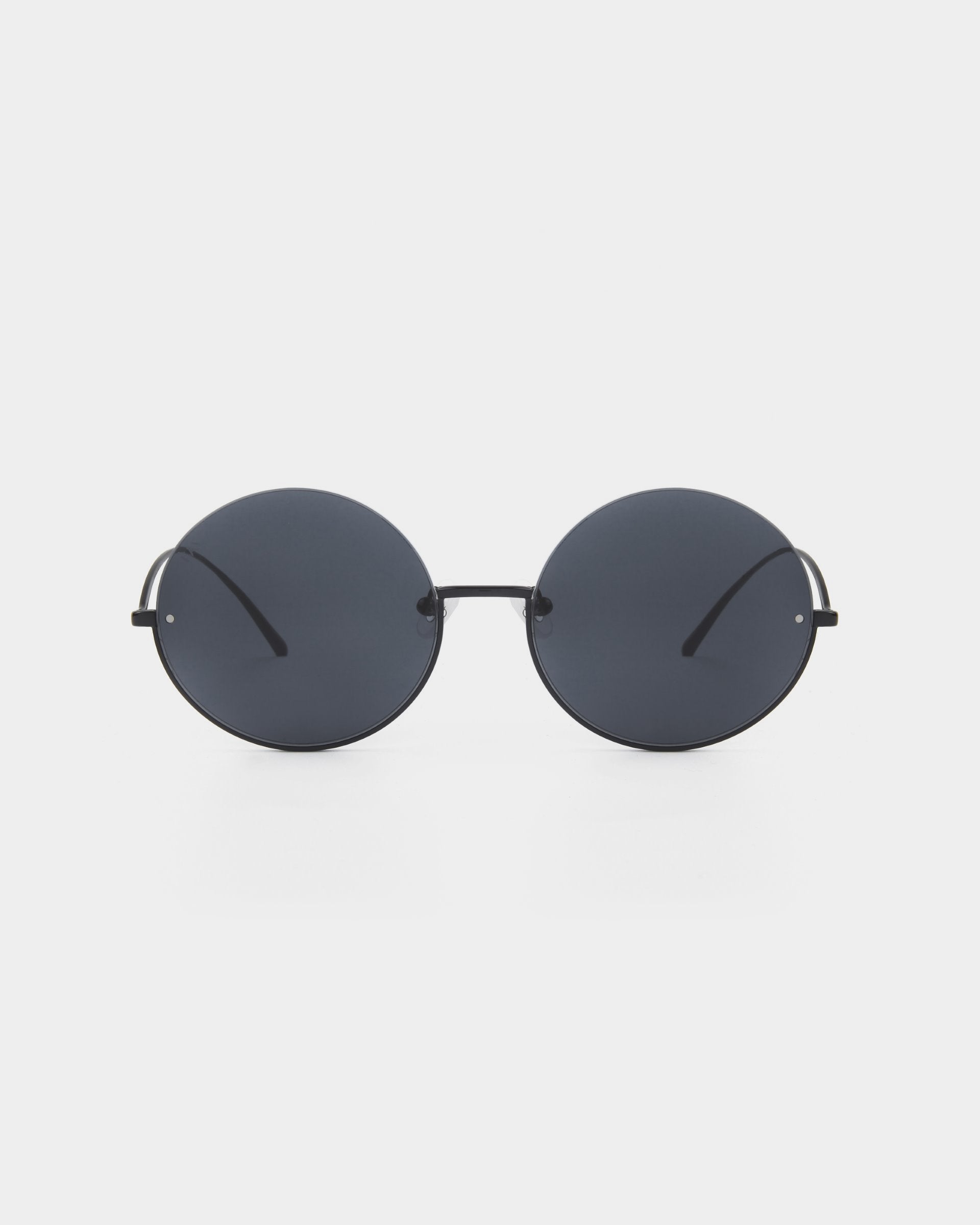 A pair of round, dark-tinted For Art's Sake® Oceana sunglasses with thin stainless steel frames is centered against a white background. The minimalist design features simple, straight temples and nose pads, giving them a sleek and modern look while offering UVA & UVB protection.