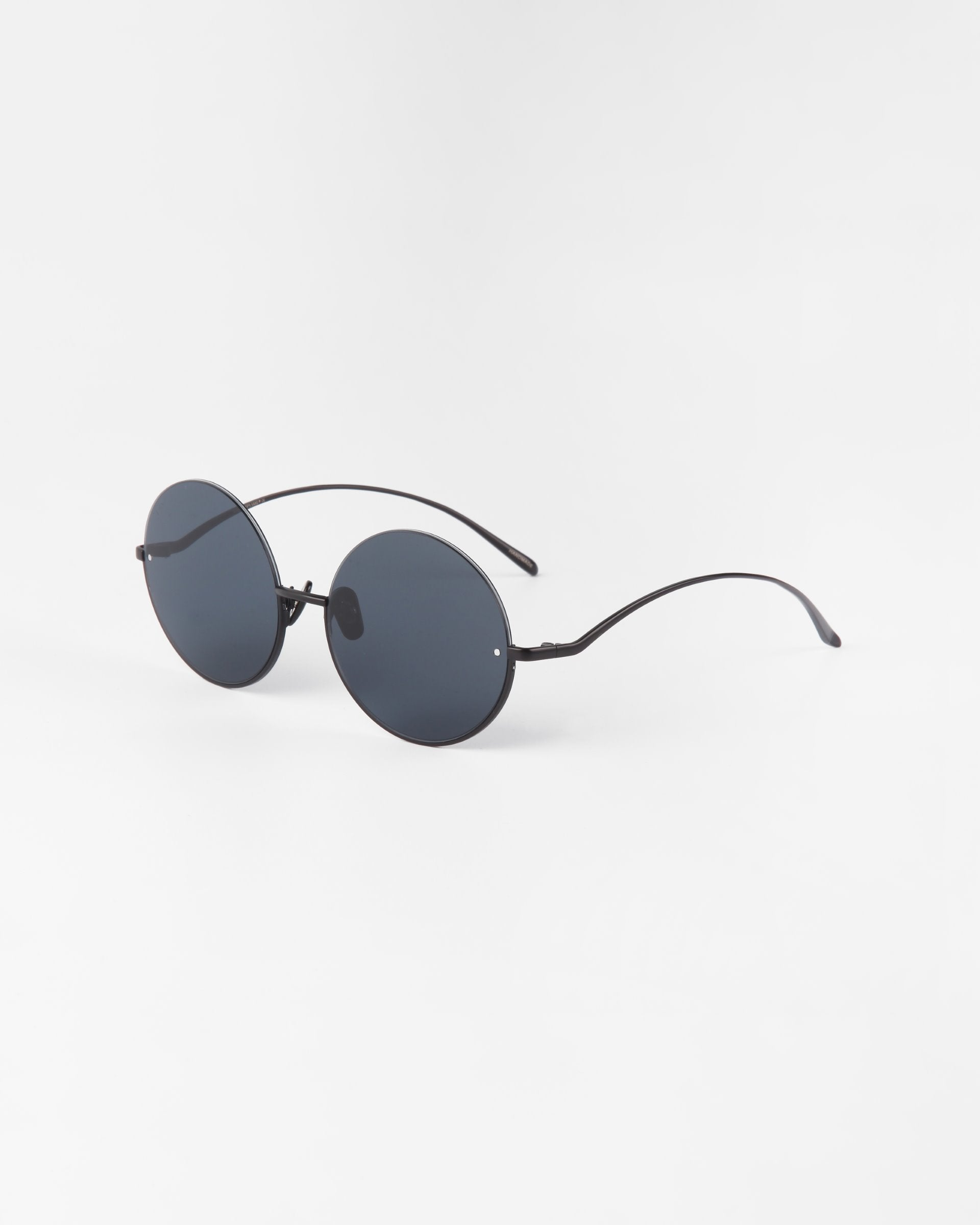A pair of Oceana sunglasses by For Art&#39;s Sake® with black nylon lenses offering UVA &amp; UVB protection and thin stainless steel arms is positioned against a plain white background.