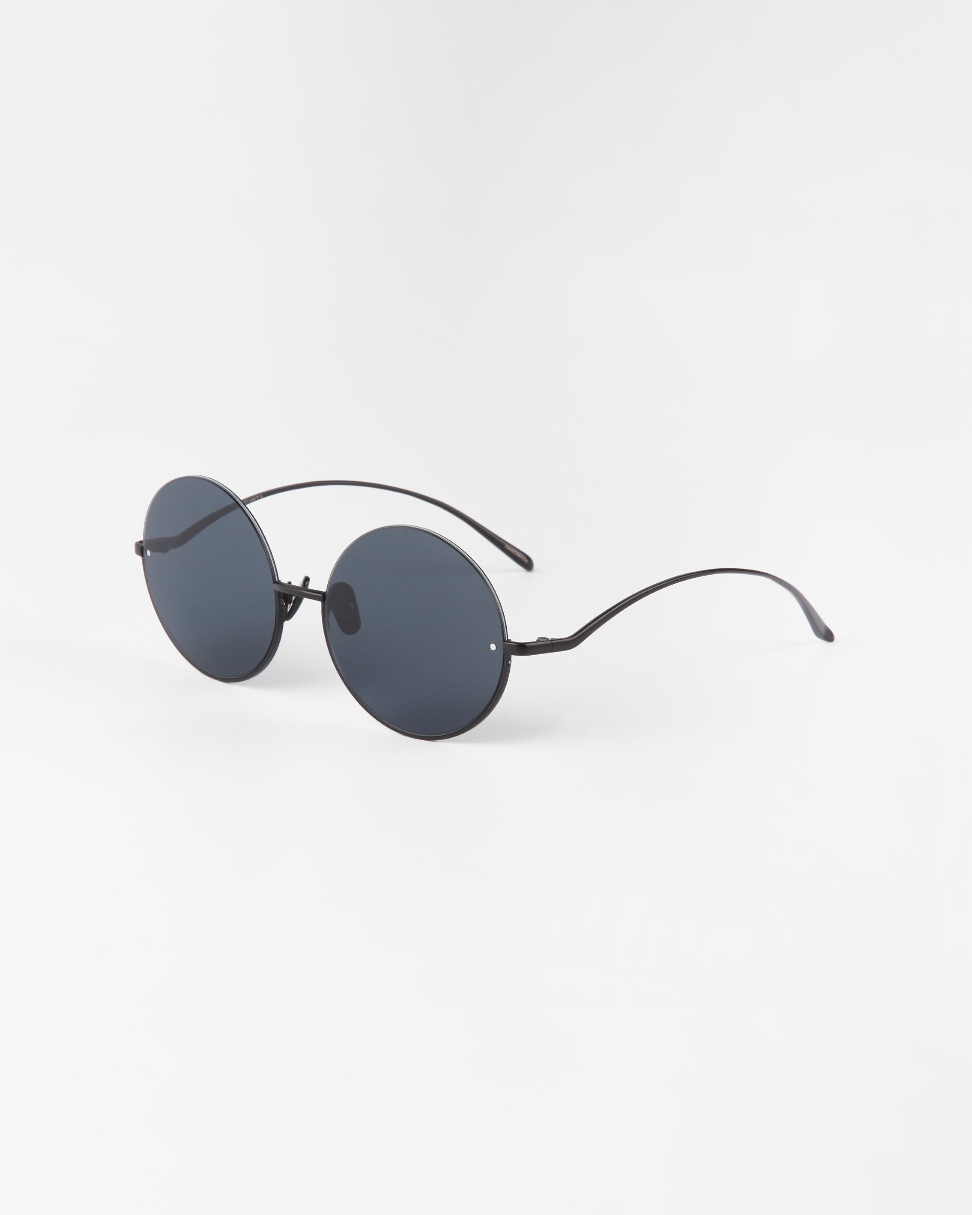 A pair of Oceana sunglasses by For Art's Sake® with black nylon lenses offering UVA & UVB protection and thin stainless steel arms is positioned against a plain white background.