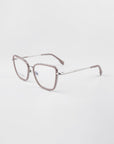 A pair of Lace eyeglasses from For Art's Sake® with transparent gray frames, thin silver temples, and a blue light filter. The lenses are clear, and the nose pads are adjustable. The background is solid white, showcasing the glasses from a three-quarter angle.