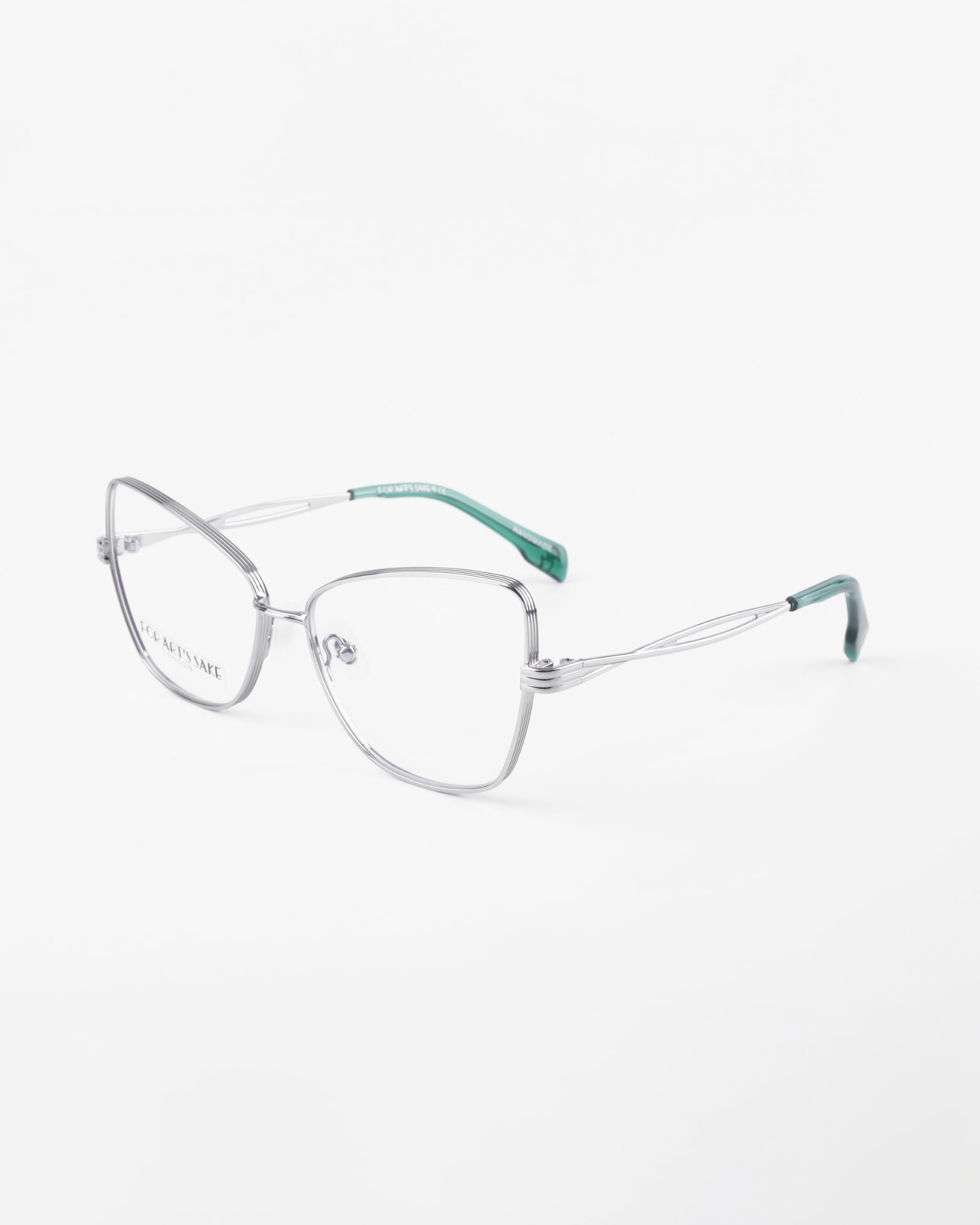 A pair of stylish eyeglasses with thin, silver metal frames and clear lenses. The temples are predominantly silver with green tips. Featuring a sleek, modern design suitable for everyday wear, the &quot;Lady&quot; frames by For Art&#39;s Sake® also offer an optional blue light filter. The background is plain white.