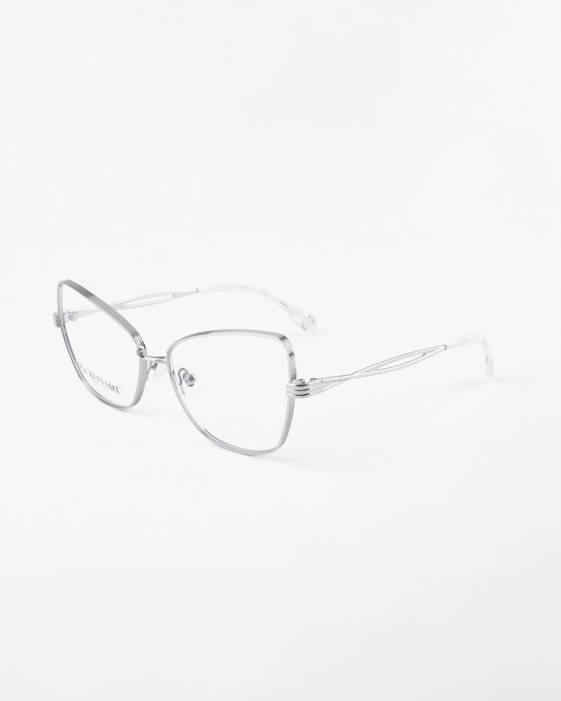 A pair of silver metal-framed eyeglasses named Lady with a minimalist design from For Art&#39;s Sake®. The glasses have thin, rectangular lenses featuring a blue light filter and delicate temple arms. The backdrop is plain white, highlighting the sleek and modern aesthetic of the eyewear.