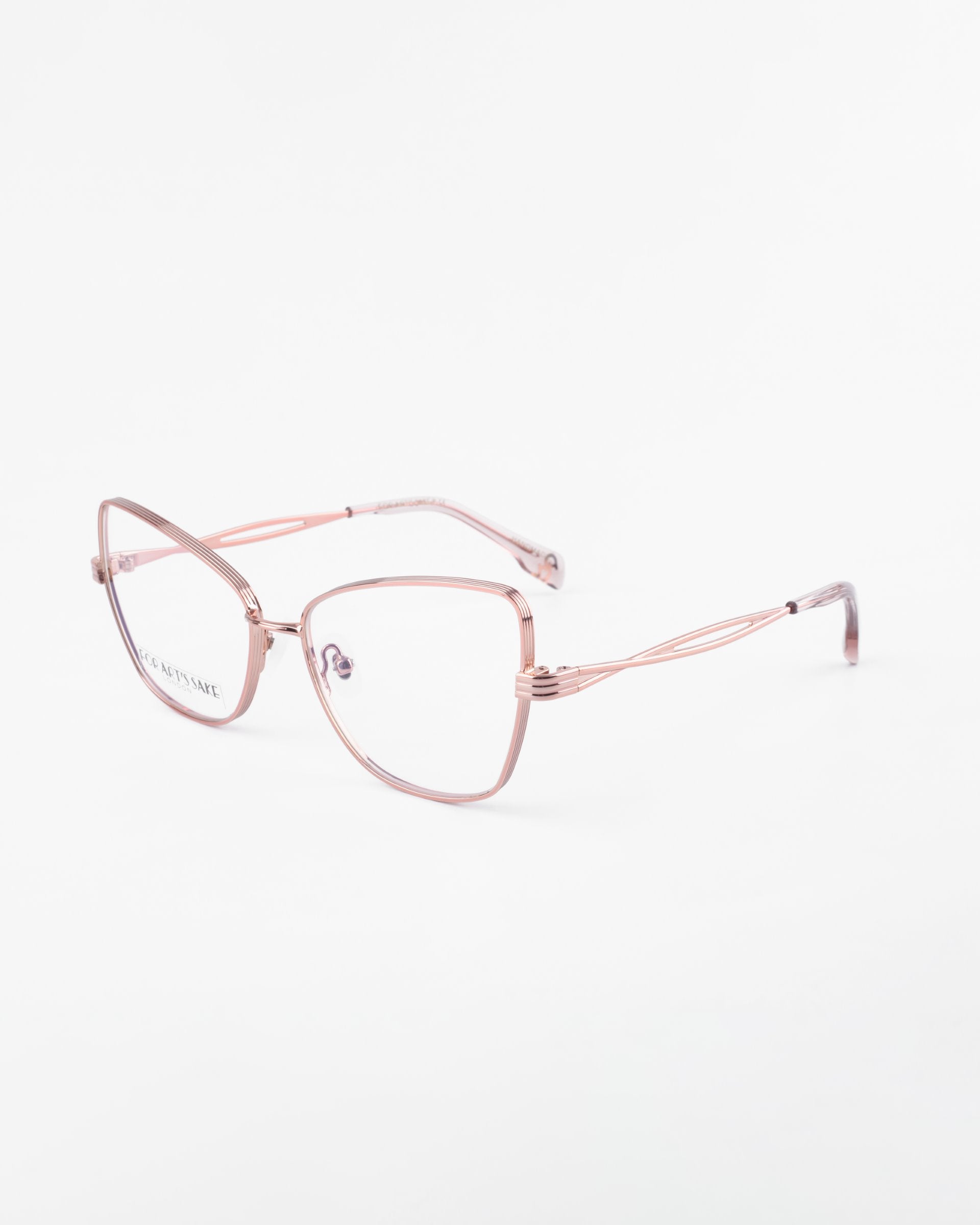 A pair of Lady eyeglasses by For Art&#39;s Sake® with thin, metallic rose gold frames and large, slightly rectangular lenses. Featuring blue light filter prescription lenses, the glasses rest on a white background, showcasing small nose pads and slender, intricately designed side temples for a modern and elegant look.