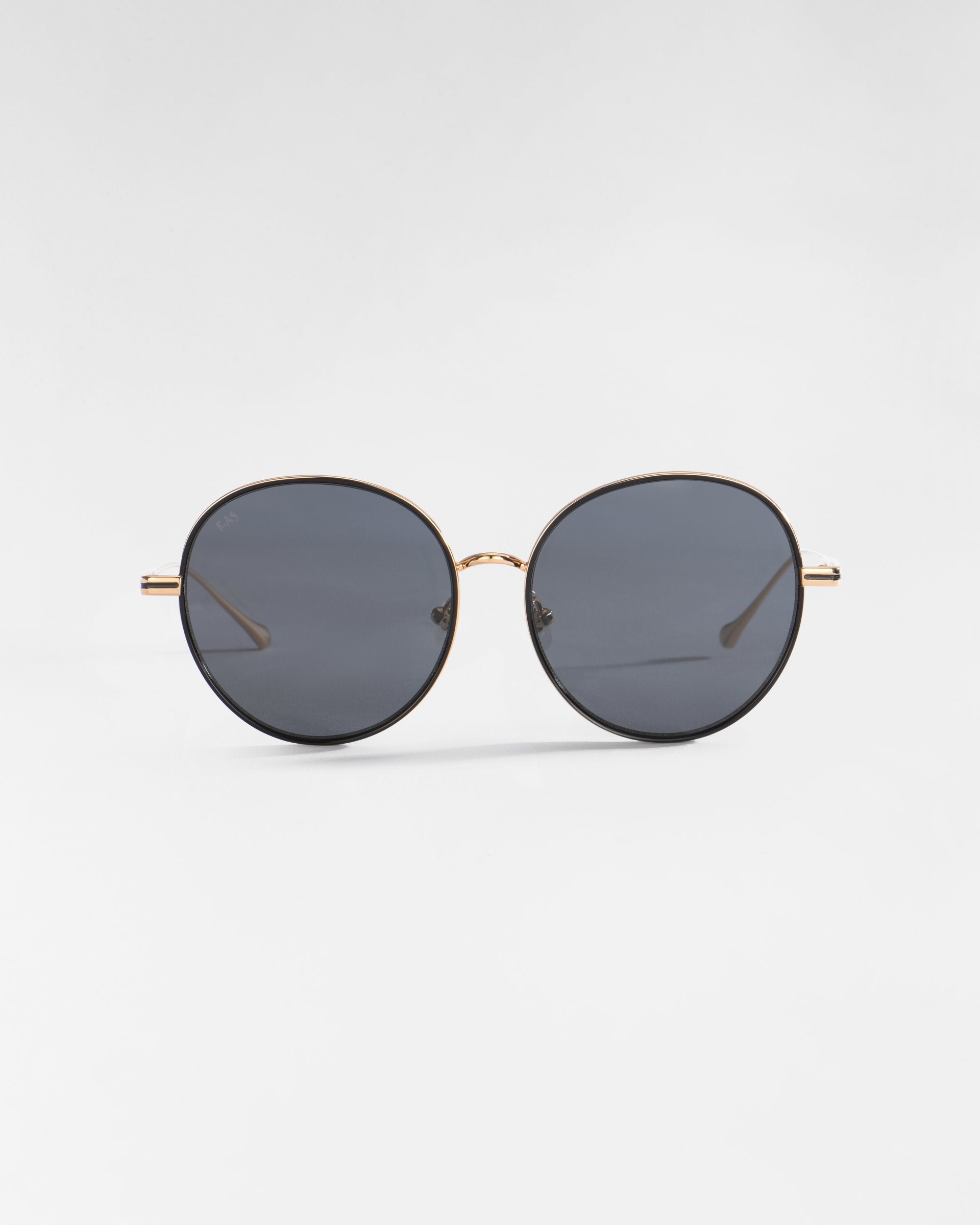 A pair of round sunglasses with thin 18-karat gold plated frames and dark grey lenses, adorned with jadestone nose pads, positioned against a plain white background. Product Name: Lemon, Brand Name: For Art's Sake®.
