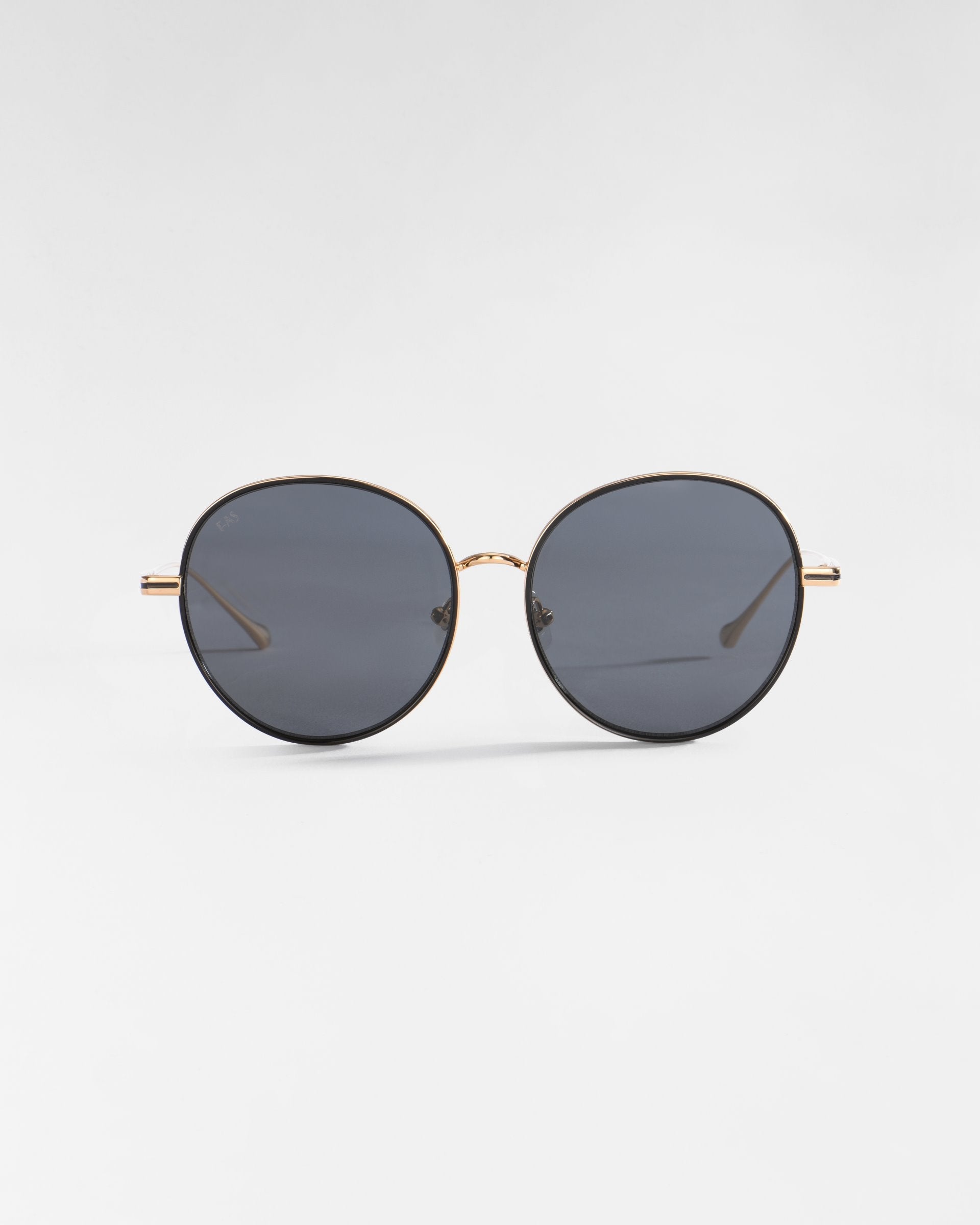 The For Art&#39;s Sake® Lemon sunglasses feature a pair of round, dark lenses and a thin gold frame, enhanced by hand-painted enamel detailing. The plain, light-colored background accentuates the stylish and minimalist design of these chic sunglasses.