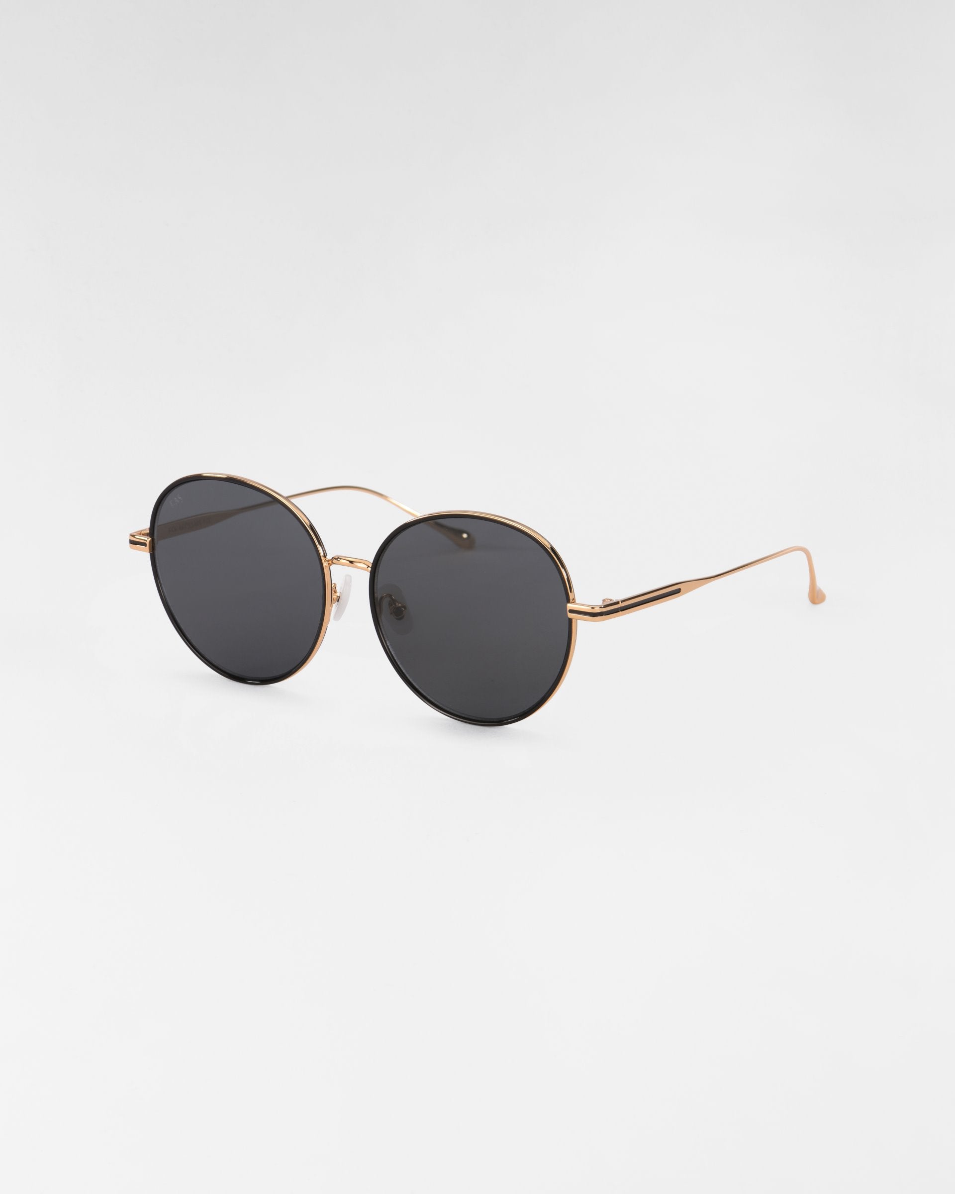 A pair of round Lemon sunglasses from For Art&#39;s Sake® with thin, 18-karat gold-plated frames and dark lenses set against a white background. The temples are slender and slightly curved at the ends, adding a touch of elegance.