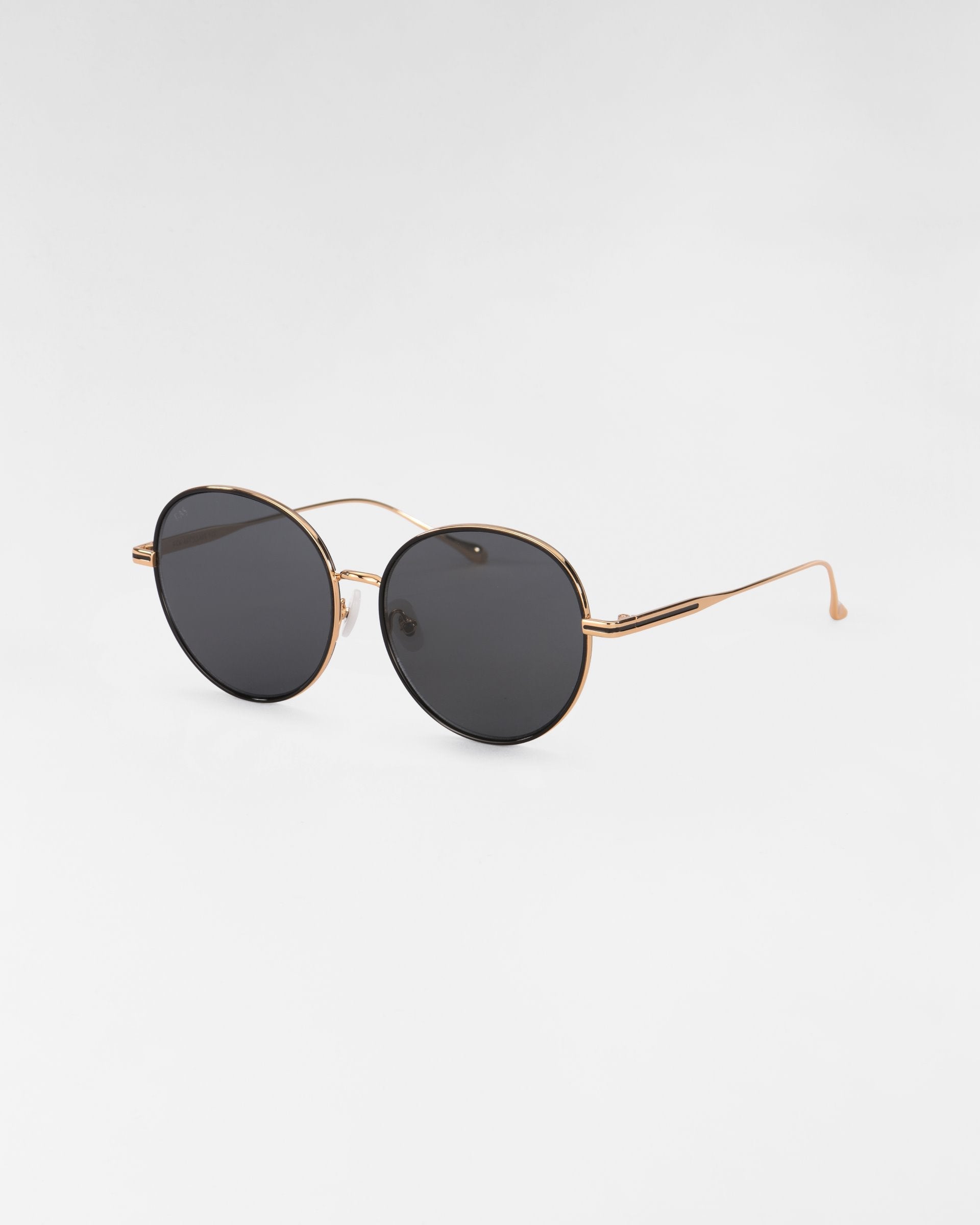 A pair of For Art's Sake® Lemon round sunglasses with black lenses and thin 18-karat gold-plated frames. The design is simple and classic, featuring slim temples and nose pads attached to the lenses. The background is plain white.