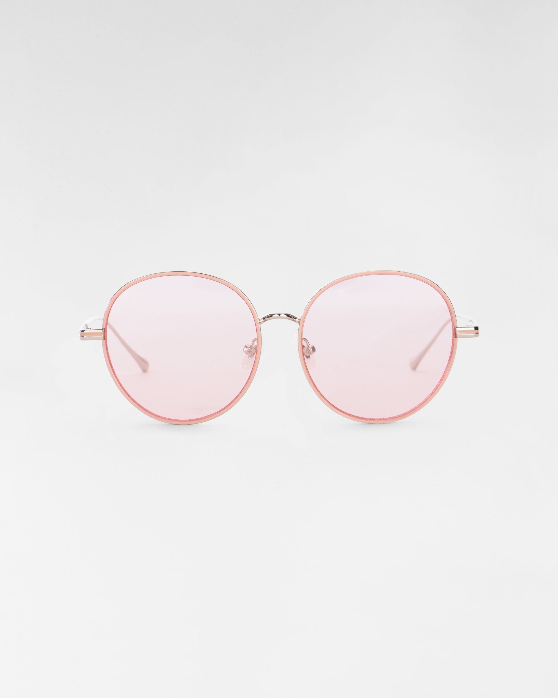 A pair of round Lemon sunglasses by For Art&#39;s Sake® with a thin, light pink metal frame and pink-tinted lenses against a white background. Featuring jadestone nose pads, the minimalist design gives a stylish and modern appearance.