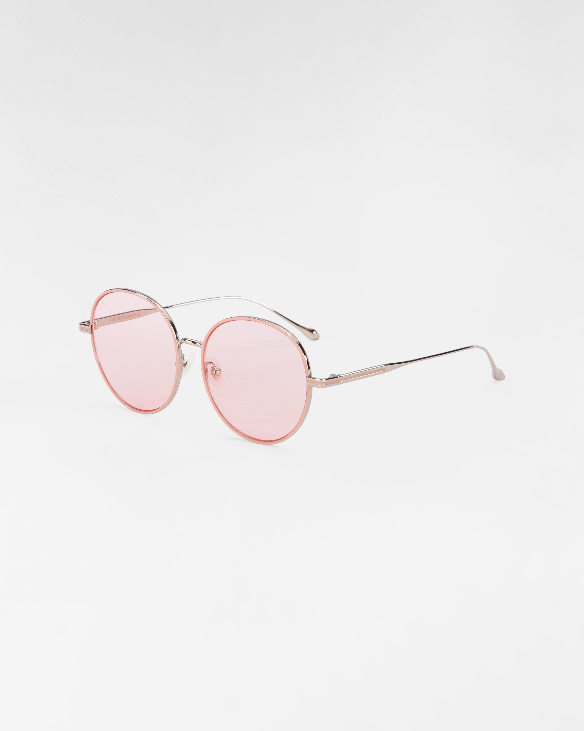 A pair of round, thin-framed For Art&#39;s Sake® Lemon sunglasses with pink-tinted lenses and metal temples. The clear nose pads are complemented by hand-painted enamel details. The frame is delicate and minimalistic, set against a plain white background.