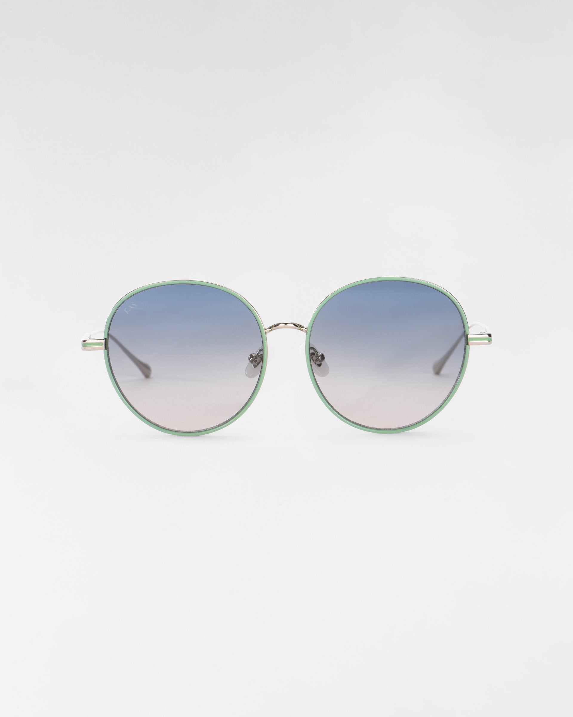 A pair of round For Art&#39;s Sake® Lemon sunglasses with green frames and blue gradient lenses is displayed against a plain white background. The temples and nose bridge are metallic, featuring 18-karat gold plating, and the earpieces extend outwards in a straight line.