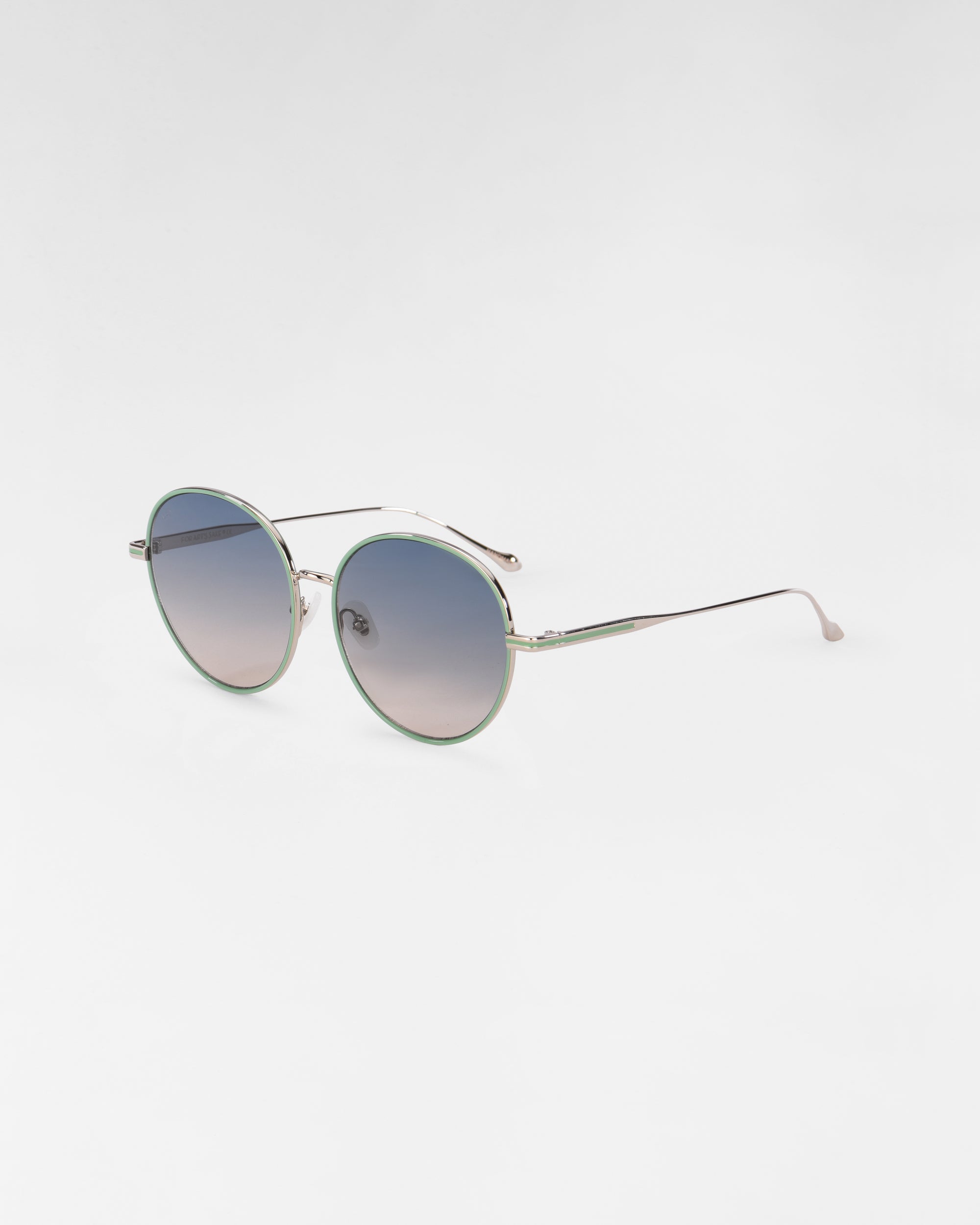 A pair of round Lemon sunglasses by For Art&#39;s Sake® featuring thin, metallic frames with 18-karat gold plating and gradient lenses that transition from dark at the top to lighter shades at the bottom. The slim temples have a slight curve at the ends for ear comfort, and Jadestone nose pads add a touch of elegance against the plain white background.