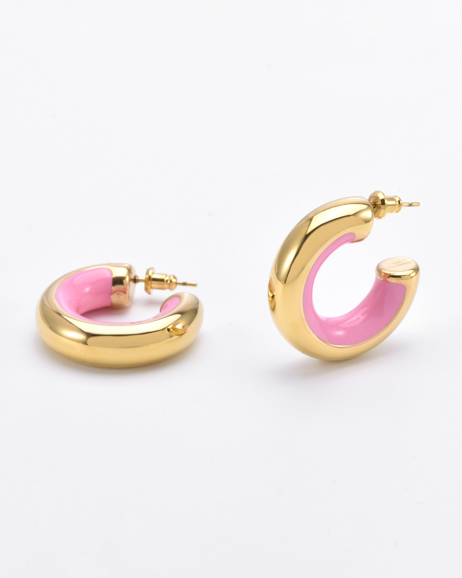 A pair of 24-karat gold-plated hoop earrings with a thick, rounded design. The exterior is gold, while the interior features shiny pink hand-painted enamel. The Lotus Earrings Pink by For Art&#39;s Sake® have post and clasp closures and are positioned on a plain white background.