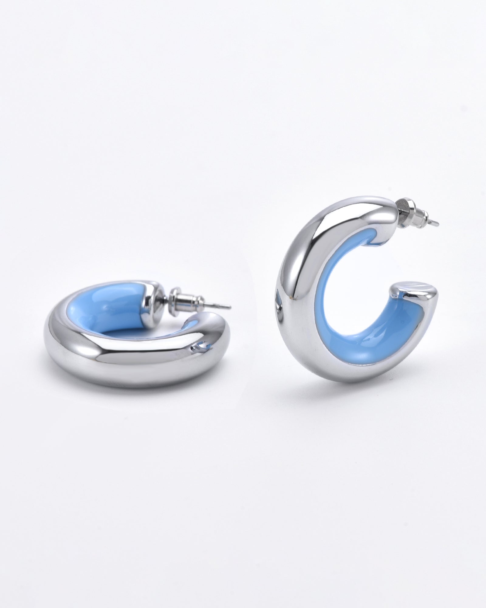 A pair of silver hoop Lotus Earrings Blue by For Art&#39;s Sake® with an inner lining of light blue are pictured against a plain white background. The 24-karat gold plated earrings are semi-circular and one is laid flat while the other is standing upright.