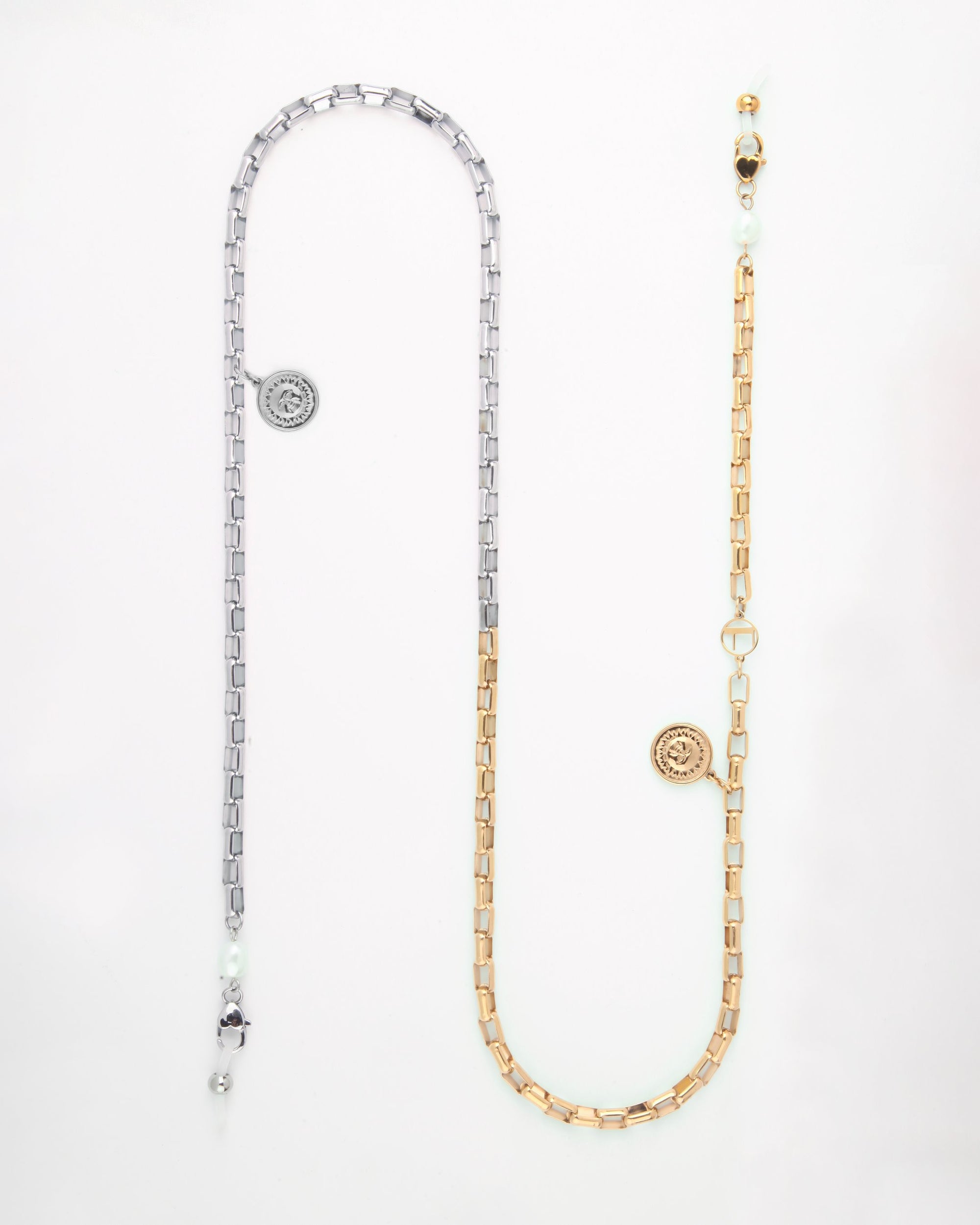A long, dual-tone glasses chain with two sections: one silver and one gold-toned metal, each featuring rectangular links. Both sections have a round pendant with an intricate design, small white pearls, and a gold circular clasp. This elegant Luna Glasses Chain by For Art&#39;s Sake® perfectly balances sophistication and style.