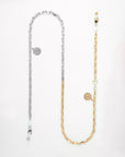 A long, dual-tone glasses chain with two sections: one silver and one gold-toned metal, each featuring rectangular links. Both sections have a round pendant with an intricate design, small white pearls, and a gold circular clasp. This elegant Luna Glasses Chain by For Art's Sake® perfectly balances sophistication and style.