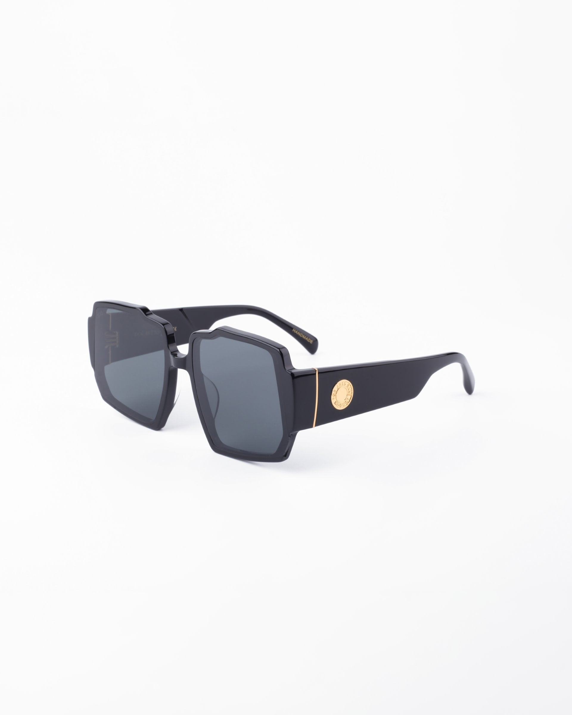 Black oversized sunglasses with chunky acetate frames, featuring gold accents on the temples. The UV-protected lenses are dark and slightly reflective. The overall style is bold and modern, suitable for fashion-forward wear. Introducing the Moritz by For Art&#39;s Sake®. The background is plain white.