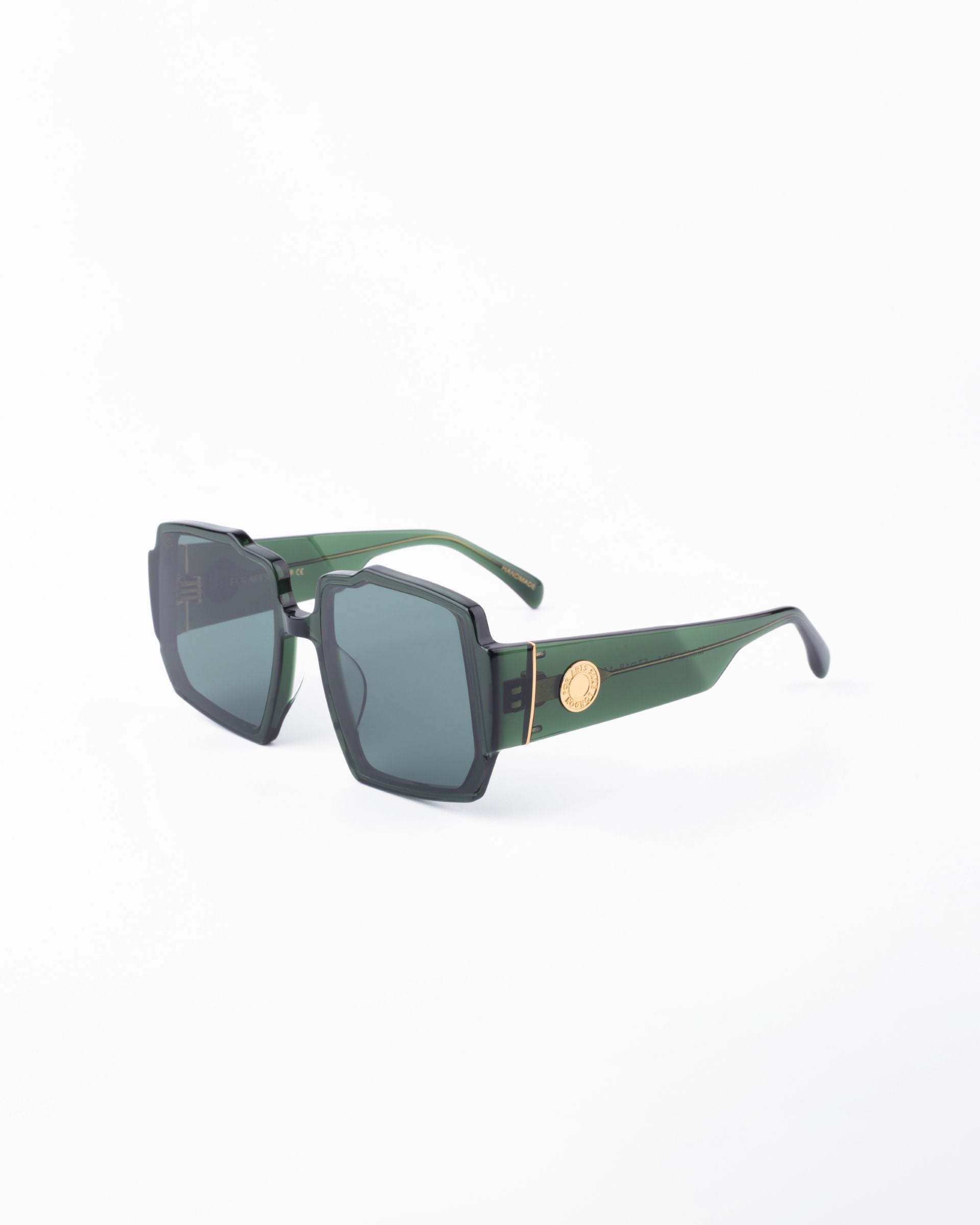 A pair of stylish sunglasses showcasing a chunky acetate frame with green hues, black UV-protected lenses, and gold-tone accents on the temples, photographed against a plain white background. The design features geometric details around the lenses. These are the Moritz by For Art&#39;s Sake®.