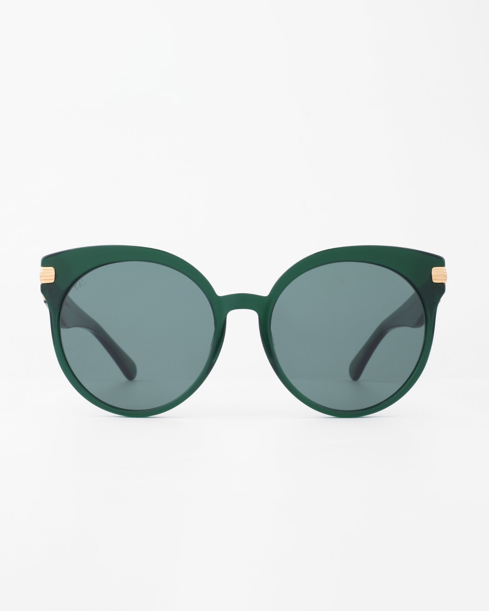 Front view of a pair of dark green round sunglasses called Muse by For Art's Sake®, with dark tinted, shatter-resistant nylon lenses. The frame boasts a sleek design made from handmade plant-based acetate, highlighted by small 18-karat gold-plated accents on the temples. The background is plain white, emphasizing the stylish eyewear.