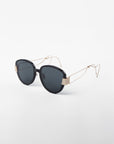 A pair of stylish Mars sunglasses from For Art's Sake® with round, dark, shatter-resistant nylon lenses and a black frame. The arms are thin, gold-plated stainless steel and intricately designed with geometric shapes. These UVA & UVB-protected Mars sunglasses are set against a plain white background.