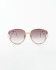 A pair of stylish For Art's Sake® Mars sunglasses with a light pink frame and gradient shatter-resistant nylon lenses that transition from dark gray at the top to lighter at the bottom. The design features square edges and metallic accents on the gold-plated stainless steel temples. The background is plain white.