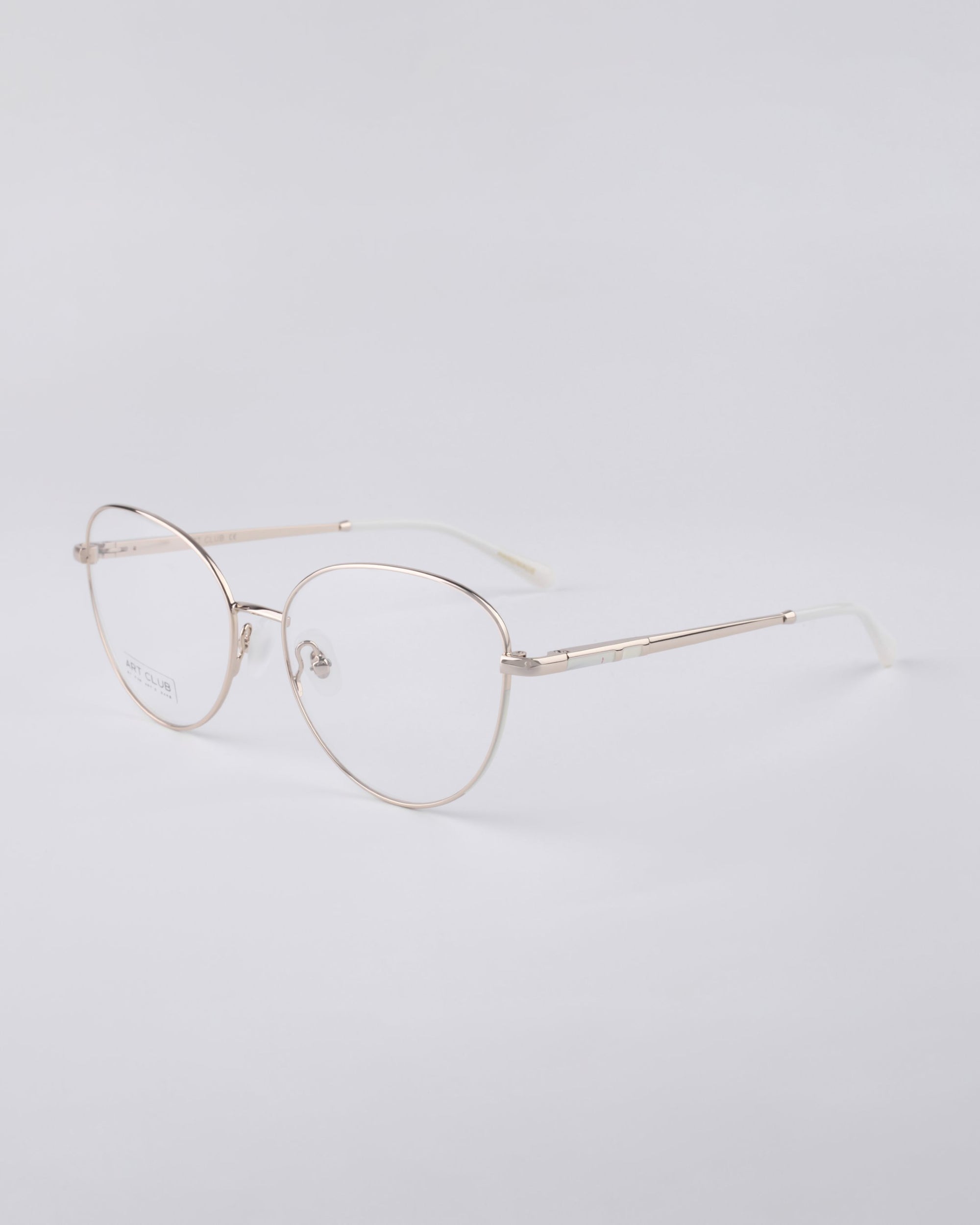 The Millie eyeglasses by For Art's Sake® are a pair of lightweight, rimless frames featuring thin, metallic gold temples and nose pads, strengthened with a stainless steel core for added durability, beautifully showcased against a neutral background.