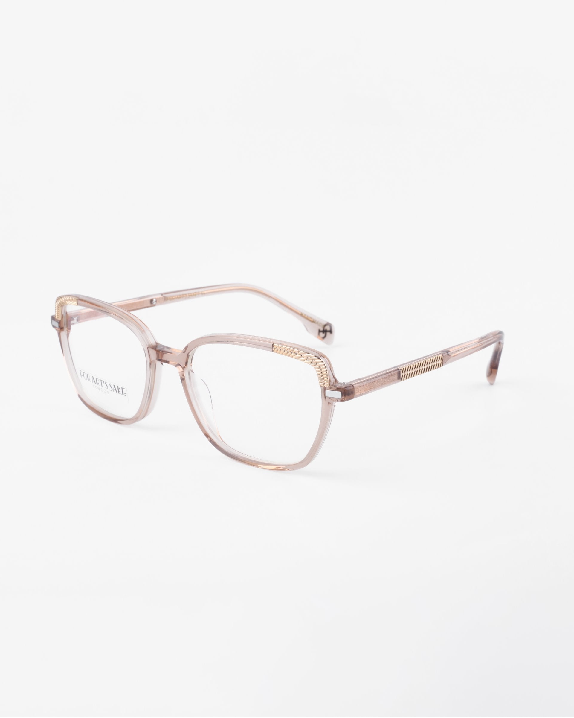 A pair of eyeglasses with a transparent pinkish-brown frame. The lenses feature a blue light filter, and the arms have a subtle golden detail near the hinges. The Mimosa by For Art&#39;s Sake®, with their gold-plated frames, are set against a plain white background.