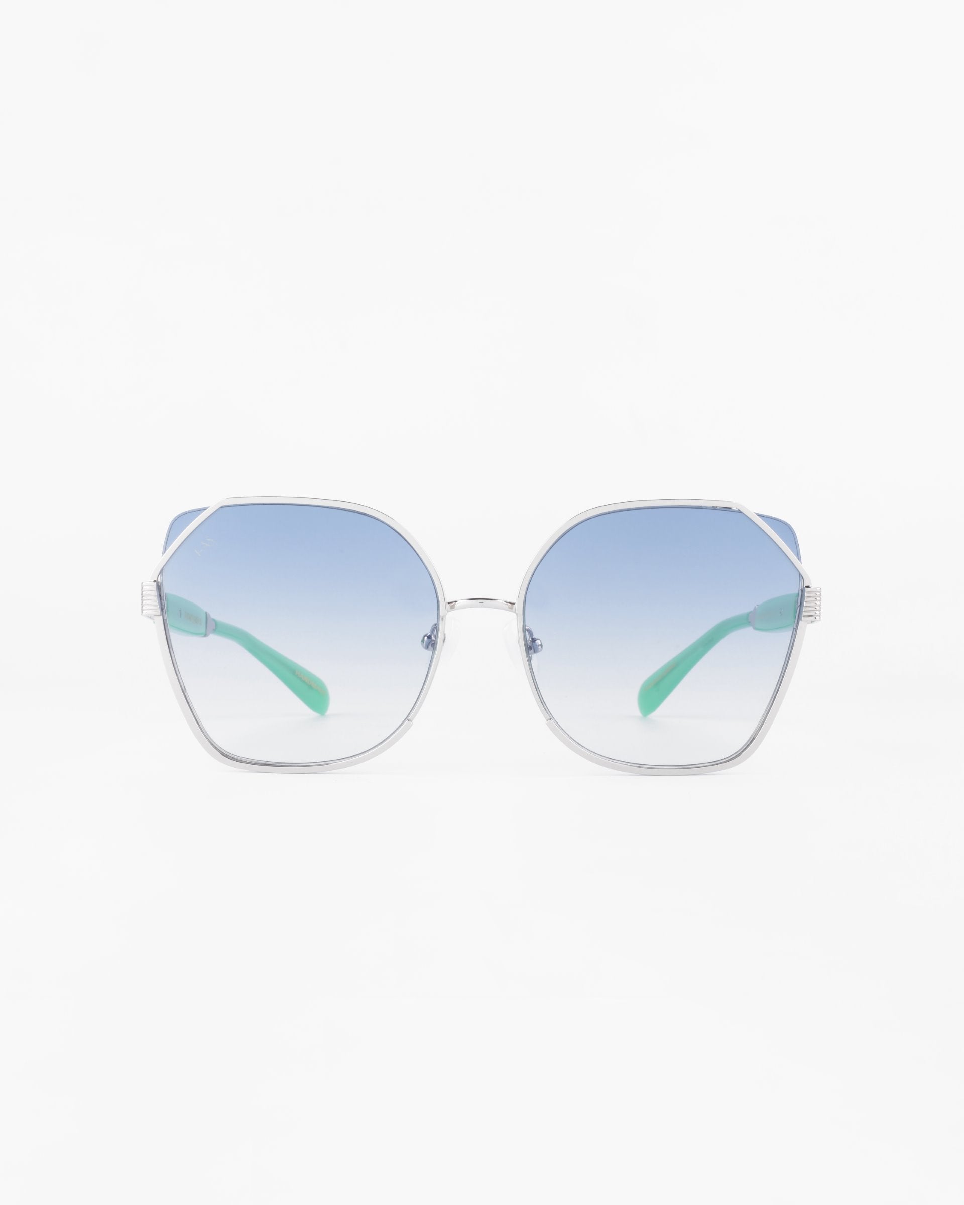 A pair of stylish sunglasses with large, hexagonal frames featuring a gold-plated stainless steel finish. The ultra-lightweight nylon lenses are gradient blue, transitioning from a darker hue at the top to a lighter shade at the bottom. The arms have a modern, sleek design with light green accents and provide 100% UVA & UVB protection. Introducing Montage by For Art's Sake®.