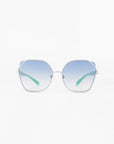 A pair of stylish sunglasses with large, hexagonal frames featuring a gold-plated stainless steel finish. The ultra-lightweight nylon lenses are gradient blue, transitioning from a darker hue at the top to a lighter shade at the bottom. The arms have a modern, sleek design with light green accents and provide 100% UVA & UVB protection. Introducing Montage by For Art's Sake®.