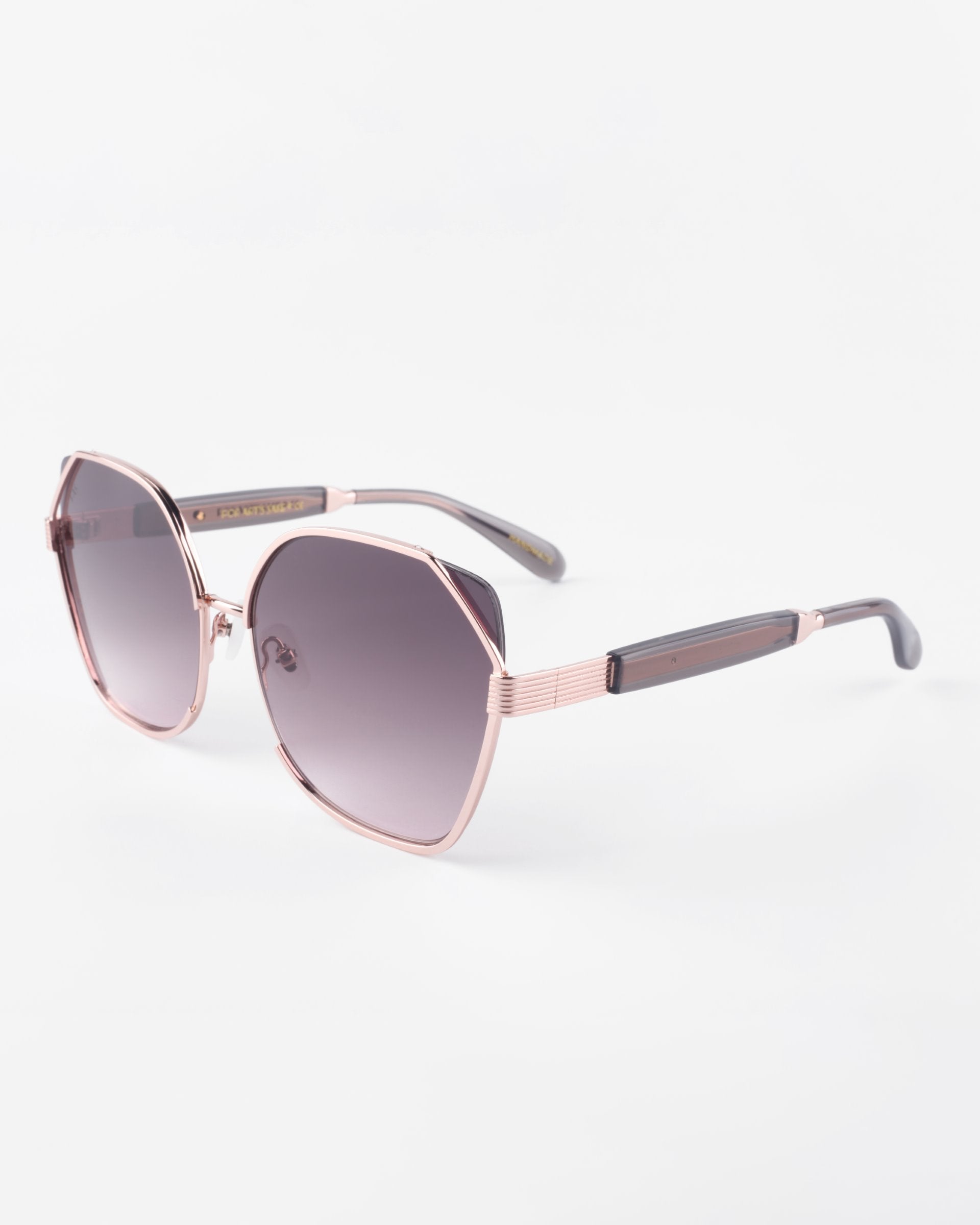 A pair of stylish Montage sunglasses from For Art's Sake® with a rose gold frame and gradient dark lenses, offering 100% UVA & UVB protection. The glasses have geometric, slightly squared lenses and sleek arms with dark tips. Made from gold-plated stainless steel, their design is modern and elegant. The background is plain white.