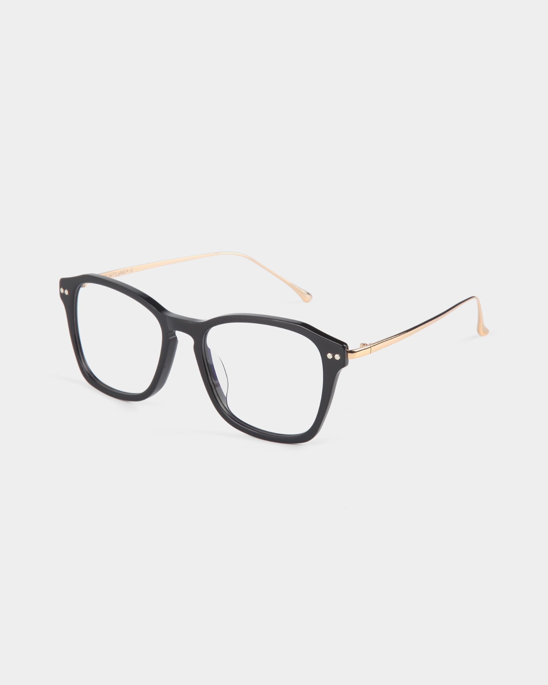 A pair of eyeglasses with matte black rectangular frames and thin metallic gold temples. The ends of the temples are rounded for added comfort. Made with stainless steel frames, these glasses also feature a blue light filter. Displayed on a clean white background, this is the Morris by For Art's Sake®.