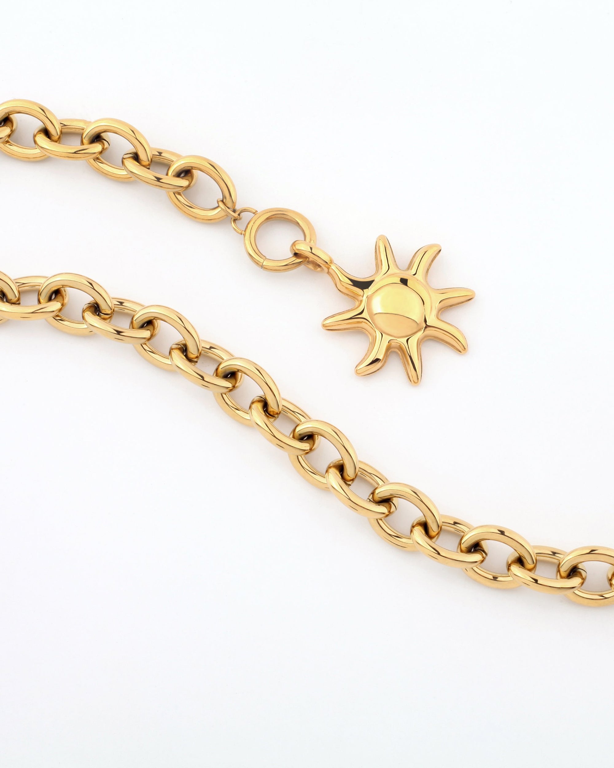 The Crescent Moon Necklace by For Art&#39;s Sake® features a series of interlocking circular links and a celestial-inspired sun-shaped gold pendant. The pendant has a smooth, round center and radiating, slightly curved rays. The necklace is arranged in a gentle curve on a plain white background.