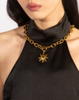 A person with long dark hair is seen wearing a black sleeveless halter neck top. They are adorned with For Art's Sake®'s Crescent Moon Necklace, showcasing celestial-inspired jewelry elegance. The background is plain and light-colored.