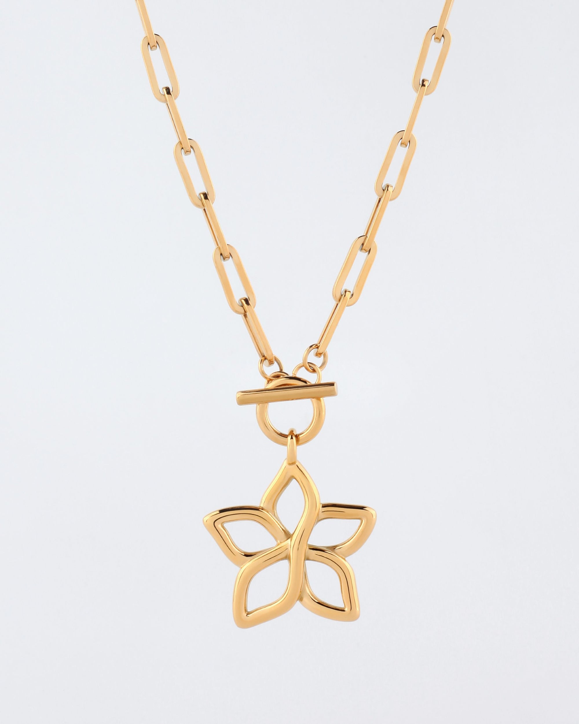 The Plumeria Necklace by For Art&#39;s Sake® is a 49cm gold necklace featuring an elongated, linked chain and a large, openwork lotus-shaped pendant hanging from a T-bar clasp. The necklace boasts a modern, minimalist design with a shiny, polished finish.