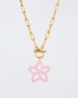 The Plumeria Necklace by For Art's Sake® features a gold chain with elongated links and a round toggle clasp that elegantly holds a pink star-shaped pendant. The five-pointed pendant boasts unique cut-out designs, giving it an airy and delicate look. Measuring 49cm in length, this piece is perfect for any occasion, especially against a plain white background.