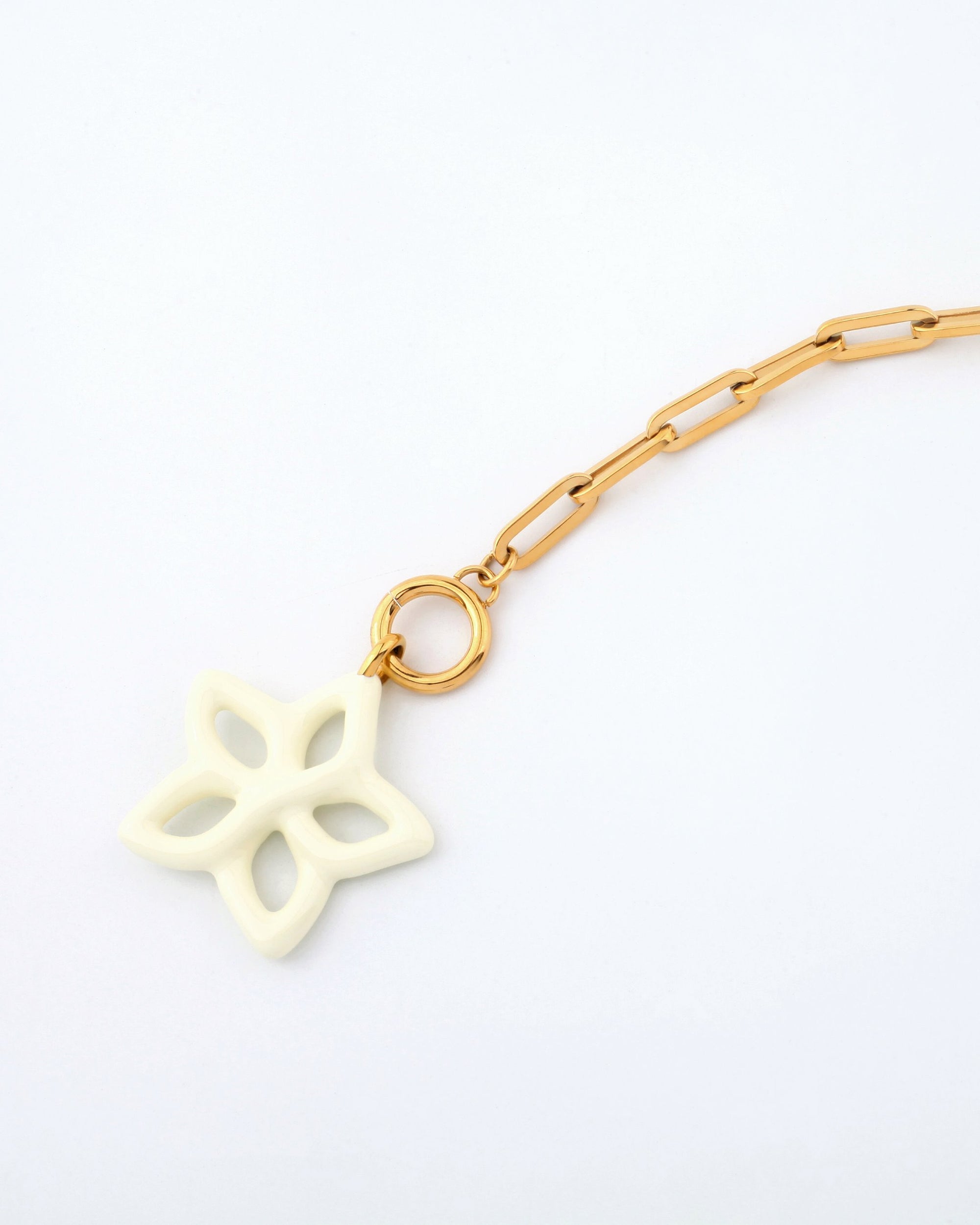 A close-up of the For Art&#39;s Sake® Plumeria Necklace, a 49cm gold chain with rectangular links, featuring a unique off-white charm shaped like a stylized, open-petaled flower. The charm is attached to the chain by a gold loop. The background is plain white.