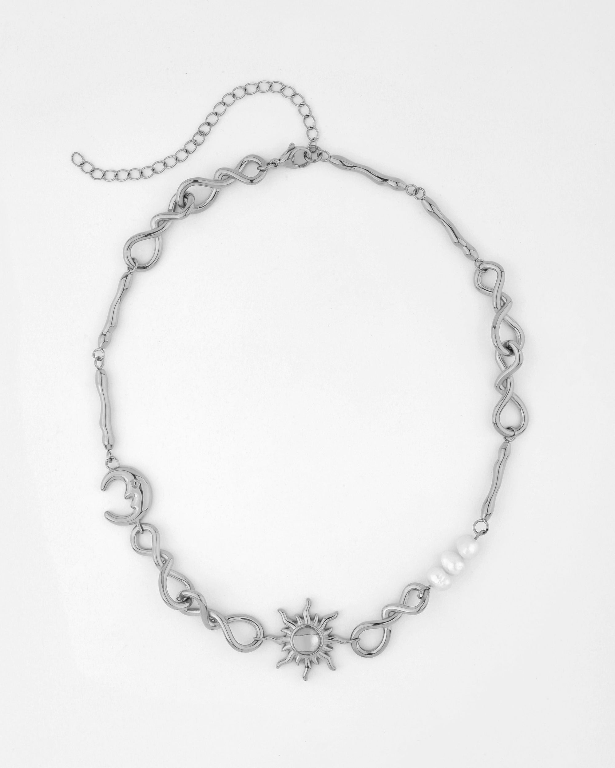 The Sloane Necklace by For Art&#39;s Sake® is a silver piece featuring an asymmetrical design with various twisted loops, a crescent moon, a sun with rays, and white pearls. It includes an extension chain for adjustable length and is shown laid flat on a white background.