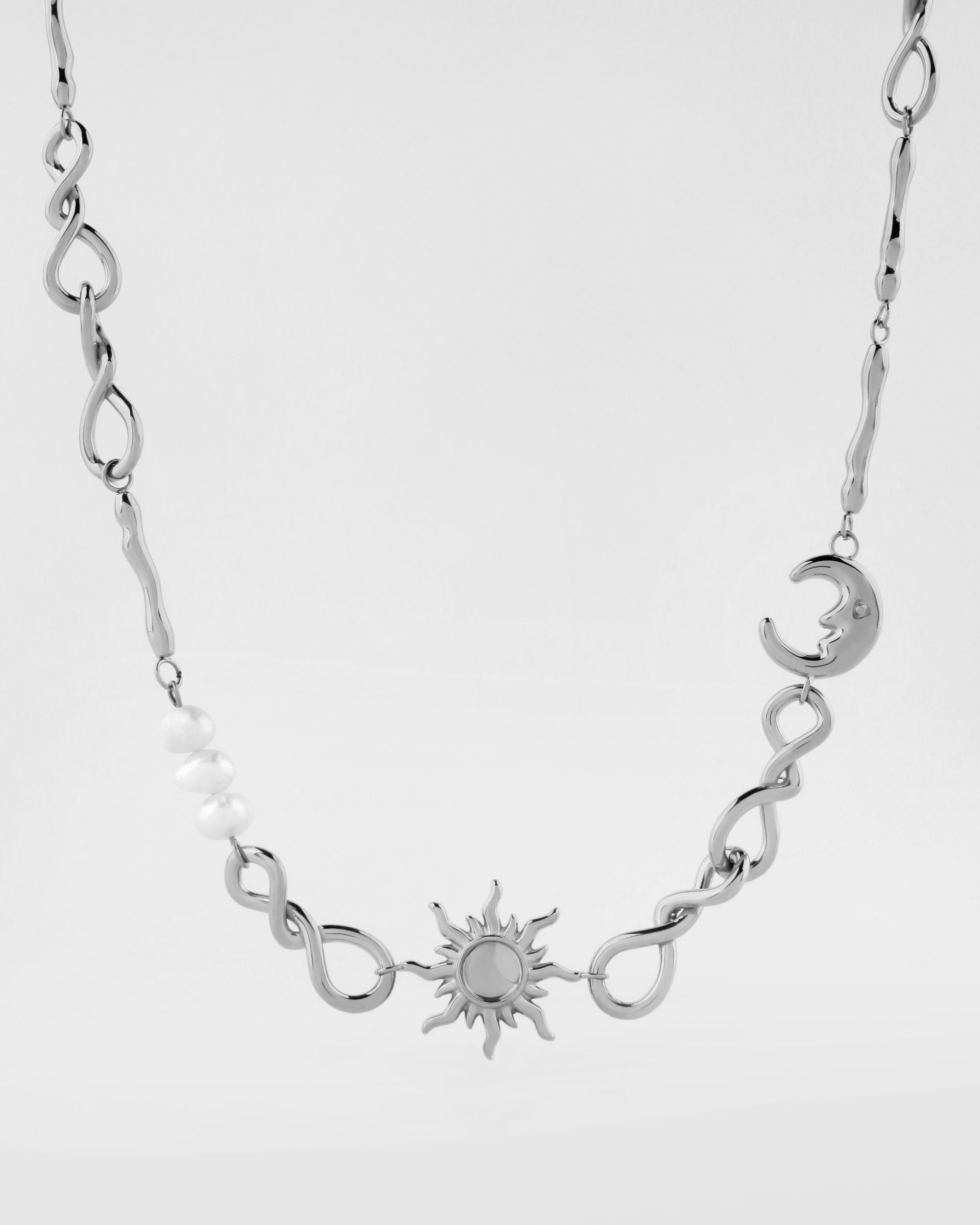 The Sloane Necklace from For Art's Sake® showcases a silver sun pendant at its center, complemented by silver loops and a crescent moon on one side. The left side of the twisted chain is adorned with several small white beads. The length of the necklace is adjustable thanks to an extension chain. It is set against a plain white background.