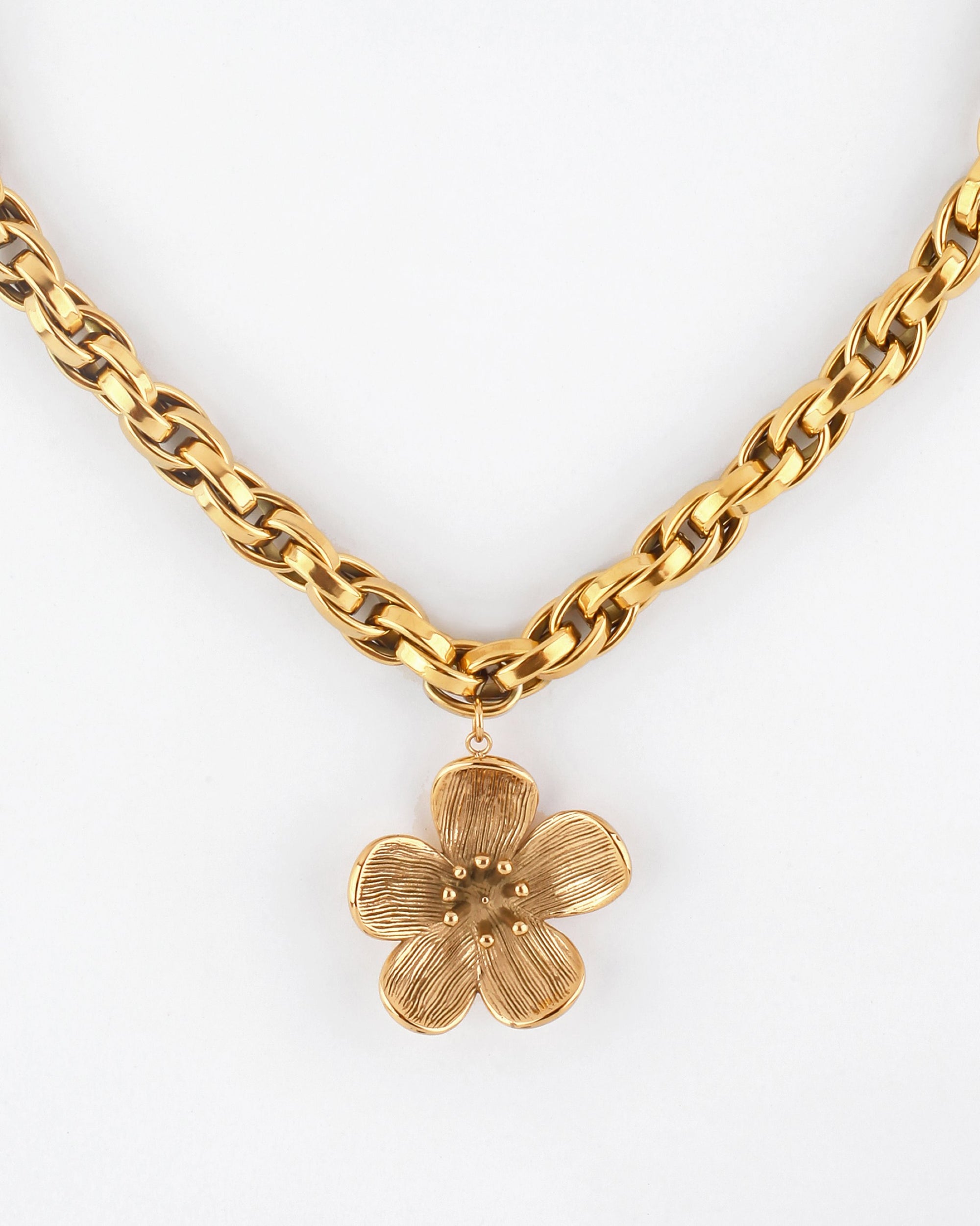 The Blossom Necklace by For Art&#39;s Sake® is a 46cm gold chain adorned with a detailed, five-petal flower pendant. The chain&#39;s interlocking links gracefully hold the pendant in the center, against a plain white background.