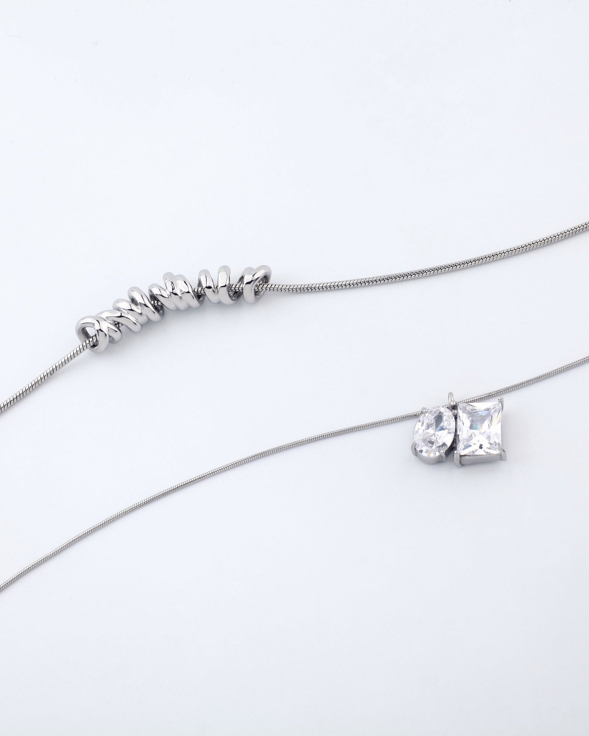 Two delicate necklaces from For Art's Sake® are displayed on a white background. The Nora Necklace features a series of small, irregularly shaped silver beads. Another necklace, also part of the Nora collection and equipped with an adjustable extension chain, showcases a pear-shaped gemstone and a square-cut gemstone side by side as its pendant.