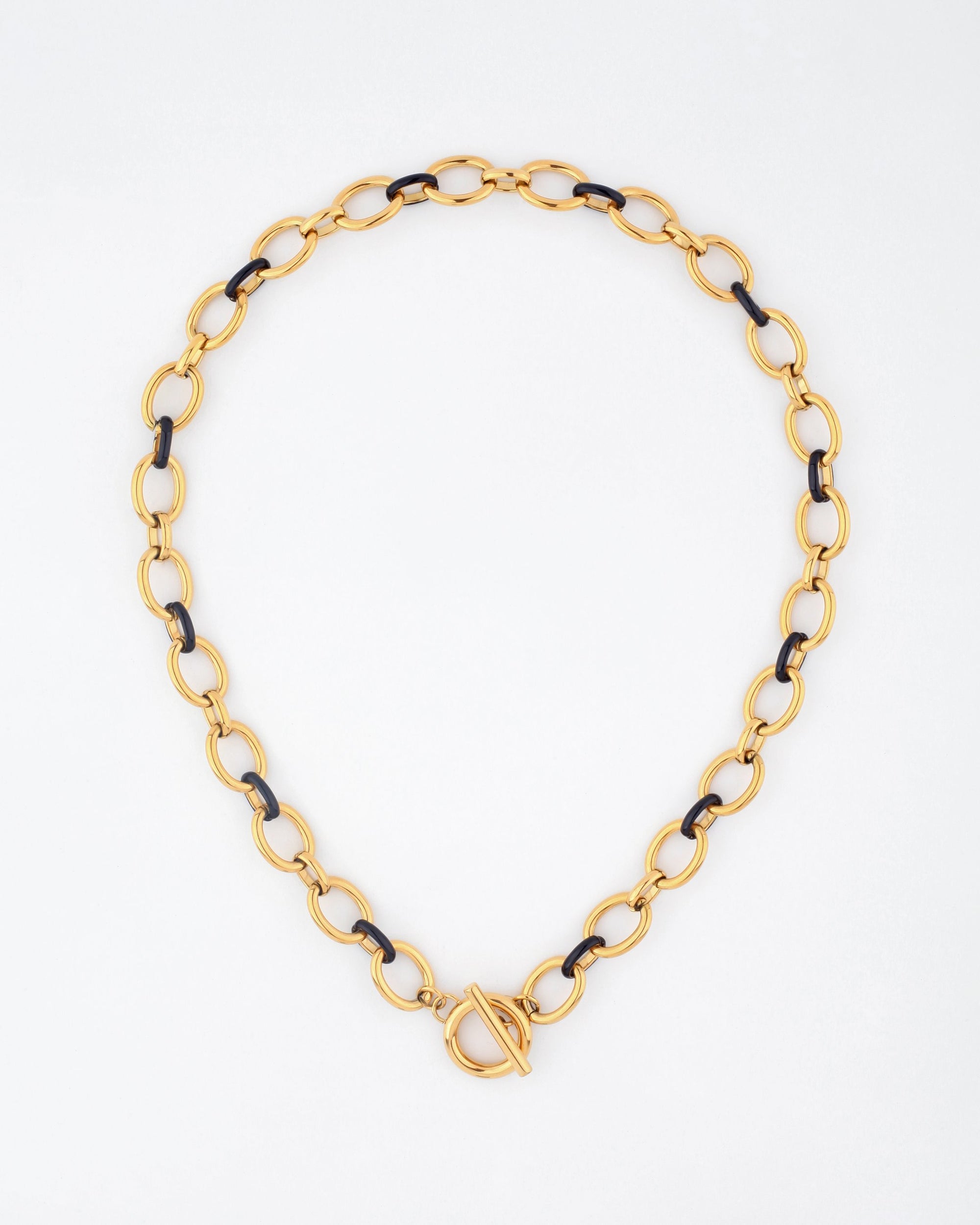 A 45cm Raya Necklace by For Art&#39;s Sake®, crafted as a gold chain with interspersed black links, featuring an oval-shaped toggle clasp centered at the front. The necklace is displayed on a light, neutral background.