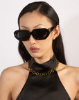 A person with long black hair is wearing large black sunglasses and a black halter top, complemented by the stylish 45cm Raya Necklace from For Art's Sake®. The plain white background accentuates their trendy outfit and accessories.