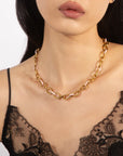 A woman wearing a delicate, strappy black lace top showcases the Raya Necklace by For Art's Sake®, featuring large interlocking gold links. The image focuses on her neck and upper chest area, highlighting the intricate design of the lace and the elegance of the 45cm length necklace.