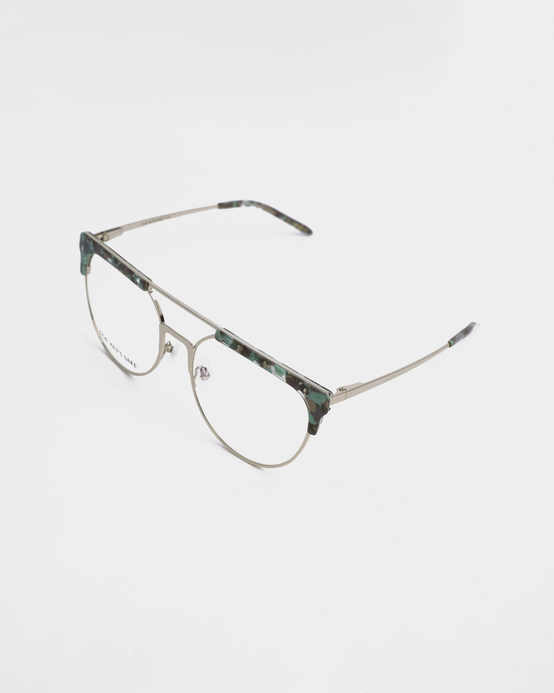 A pair of For Art&#39;s Sake® Frosty prescription glasses featuring thin metallic frames with a camouflage-patterned brow line and bridge. The earpieces are slim and also metallic, with matching camouflage accents on the tips. The clear, rectangular lenses offer both UV protection and a blue light filter for added eye comfort.