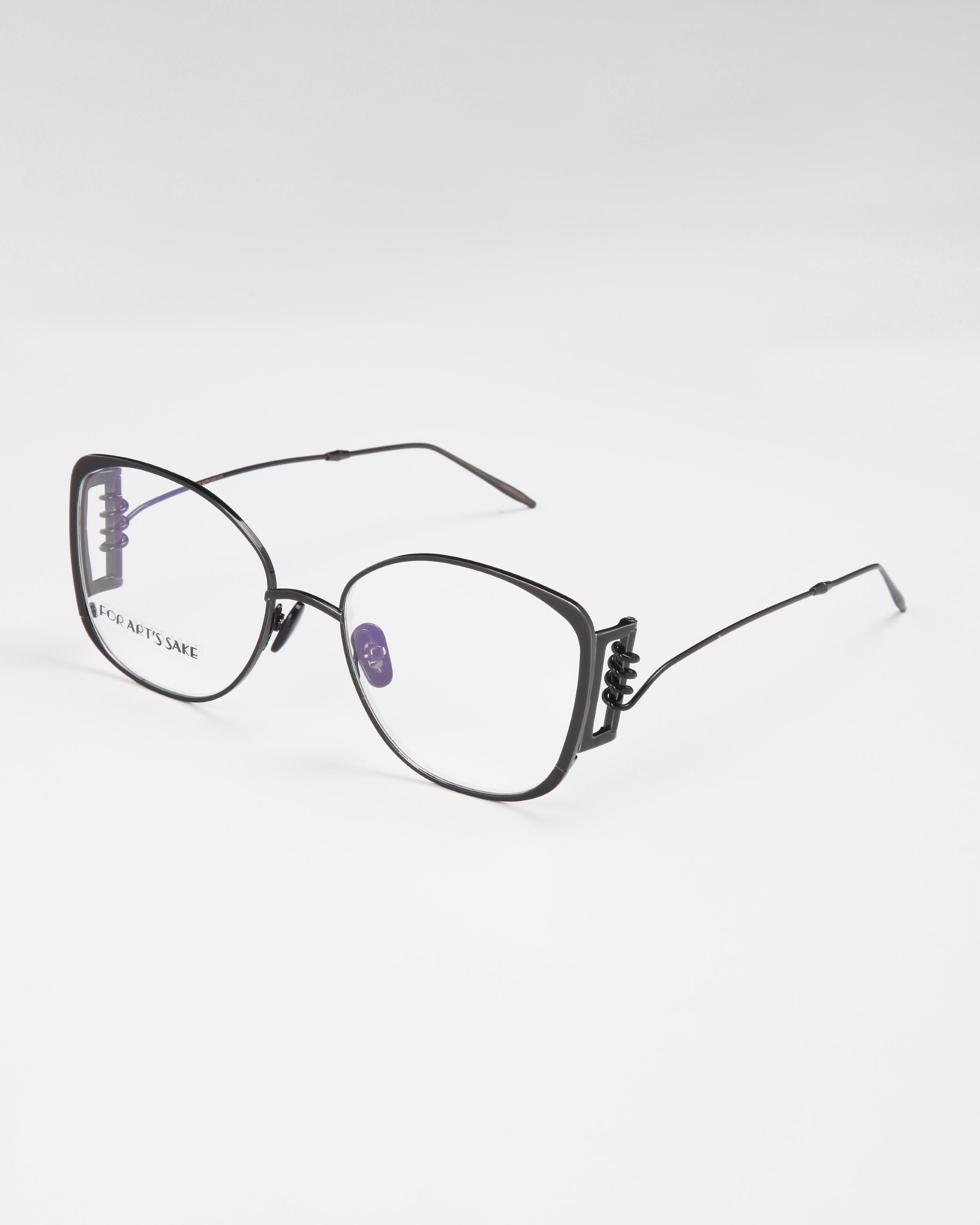 A pair of For Art's Sake® Jupiter black metal eyeglasses with large square lenses sits on a white surface. The frame has thin arms and a slight double bridge design with a small decorative element near the hinges. Featuring blue light filters, the lenses are clear, and the overall design is minimalistic yet stylish.