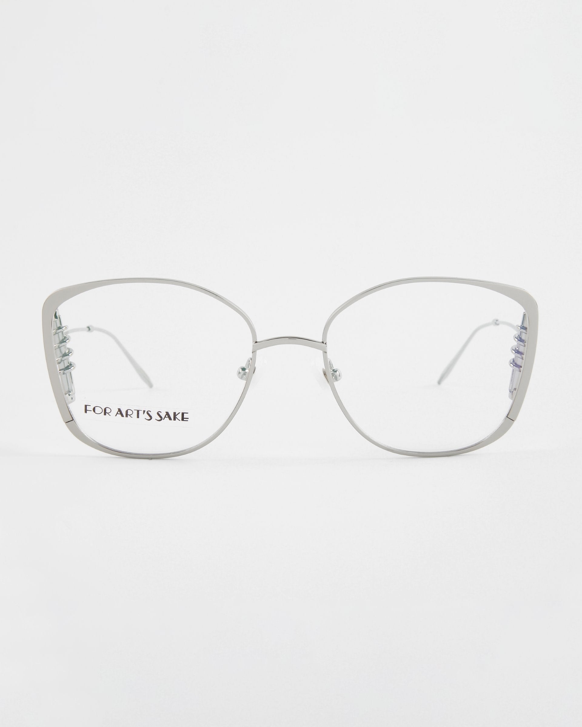 Front view of a pair of eyeglasses with silver metal frames and clear lenses featuring an 18-karat gold plating. The brand name &quot;For Art&#39;s Sake®&quot; is visible on the left lens. The design is minimalist with subtle cat-eye corners and a thin bridge. The background is plain white. These are the Jupiter model.