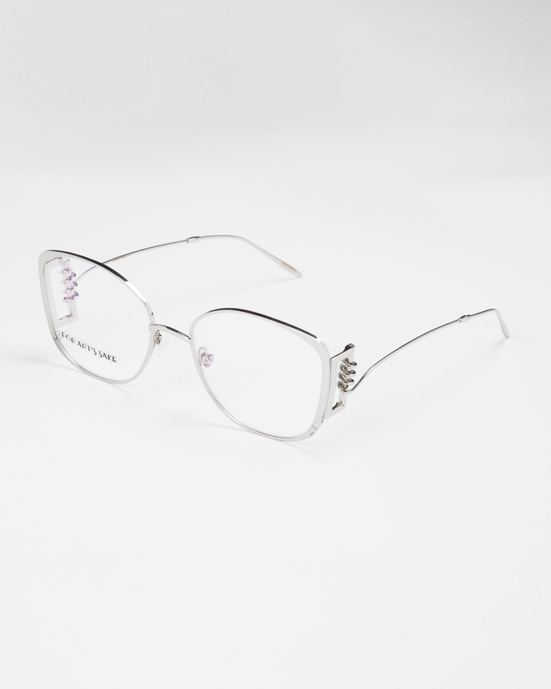 A pair of stylish, silver-framed Jupiter eyeglasses by For Art&#39;s Sake® with slightly oversized square lenses on a white background. The temples are thin and straight, with intricate decorative elements near the hinges. These chic glasses also feature a blue light filter for added comfort during screen time.