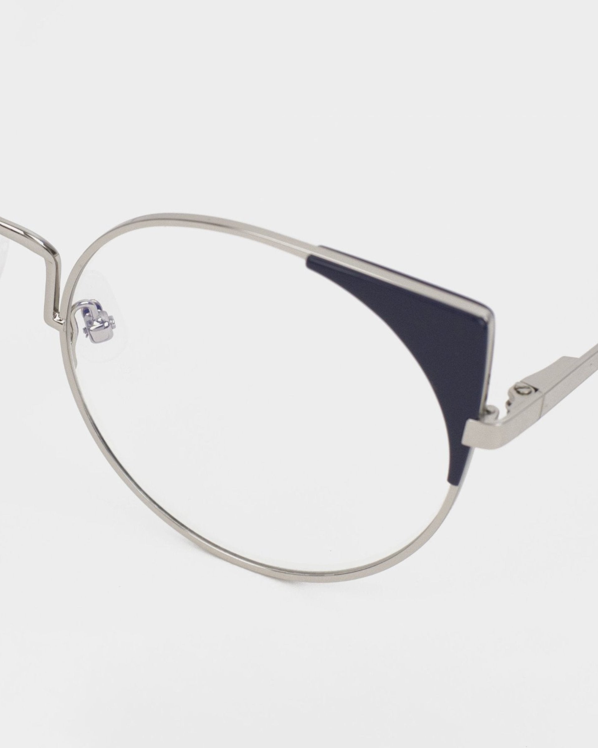 A close-up of Brisky metal-framed glasses with a cat-eye design by For Art's Sake®. The frame is silver with black accents on the upper outer corners of the lenses, featuring a blue light filter. The background is plain white, highlighting the sleek and modern design of these glasses.