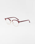 A pair of For Art's Sake® Painkiller eyeglasses with a gold wireframe and maroon-colored browline and earpieces, placed on a plain white background. The clear lenses include UV protection, enhancing the modern, sophisticated design.