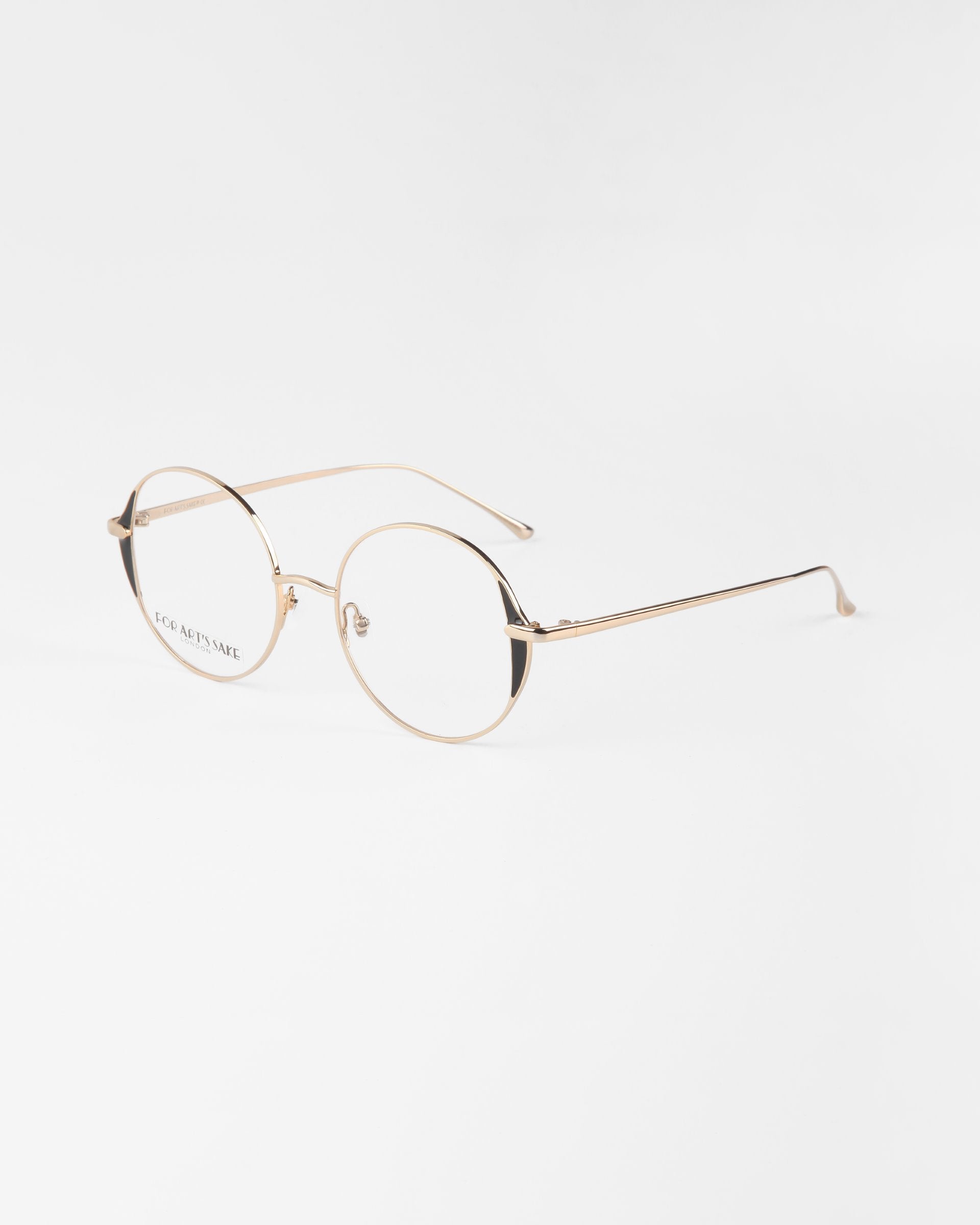 A pair of round, gold-rimmed eyeglasses with thin metal frames and clear lenses on a white background. The delicate design, featuring 18-karat gold plating, includes slim temples and bridge, giving the glasses a minimalist and elegant appearance. These are the Kos eyeglasses by For Art's Sake®.