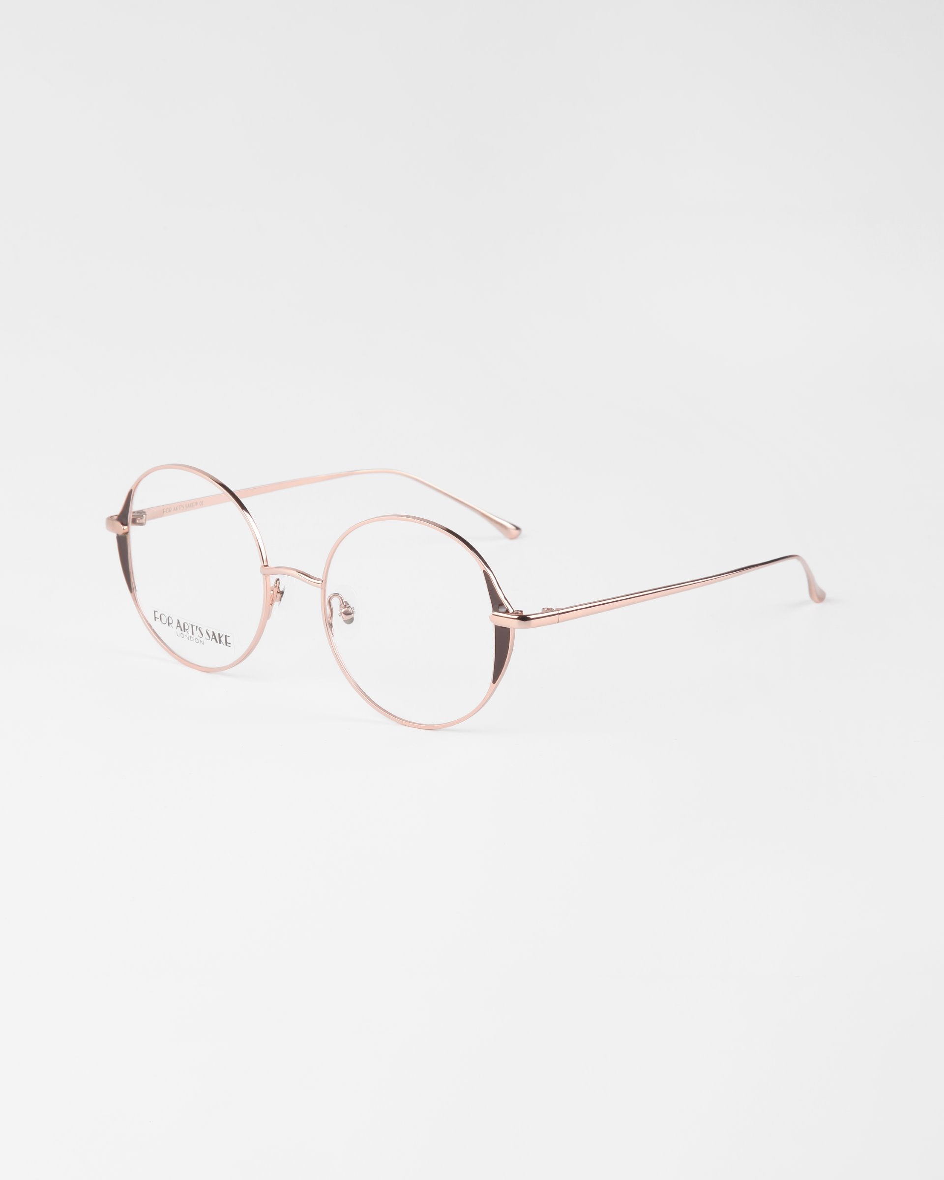 A pair of round, thin-framed, gold-rimmed eyeglasses with clear lenses and 18-karat gold plating. The design is minimalist, with delicate frames and no visible embellishments on the glasses. The glasses are called Kos by For Art's Sake® and are placed on a plain white background.